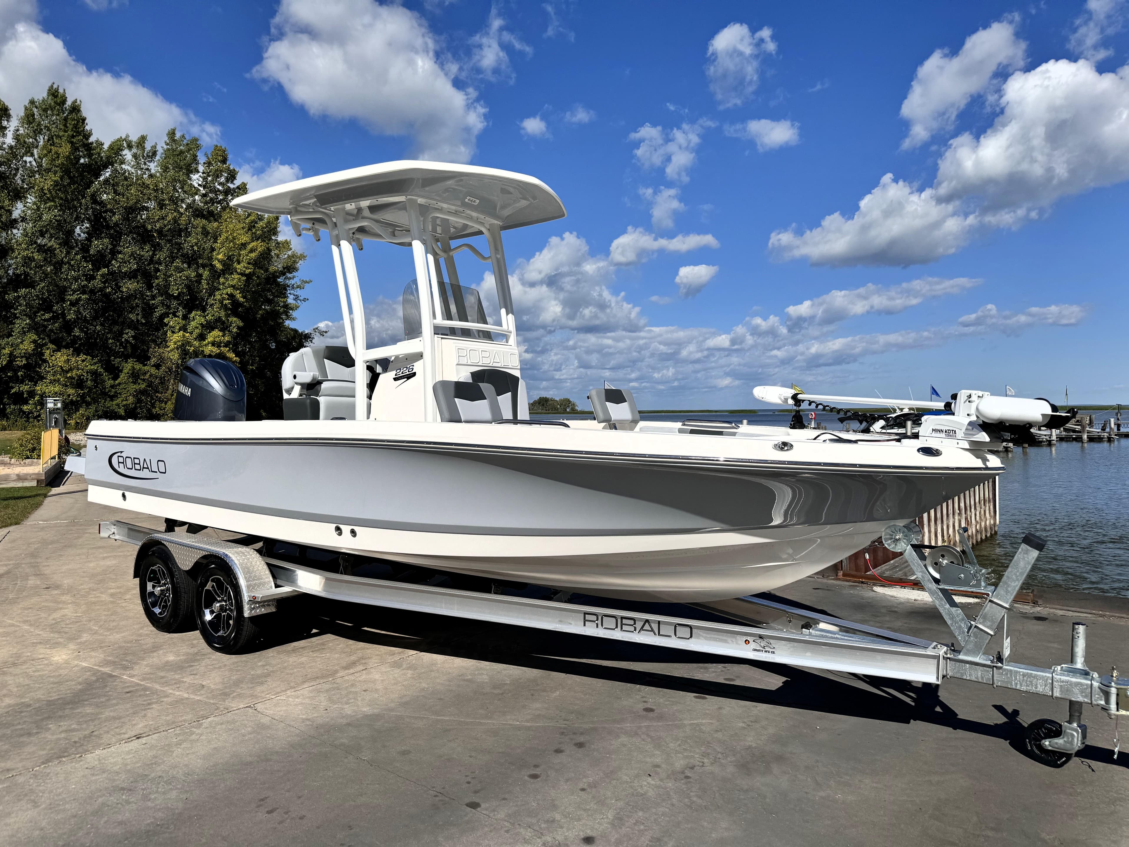 2025 Robalo 226 Cayman boat on trailer by a lake under blue sky.