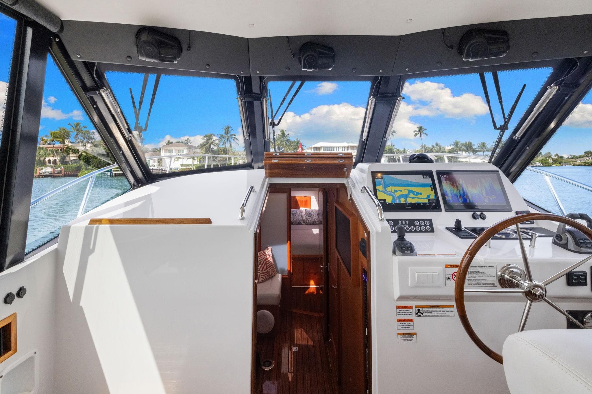 2024 MJM 42 yacht cockpit with navigation screens, steering wheel, and scenic water view.
