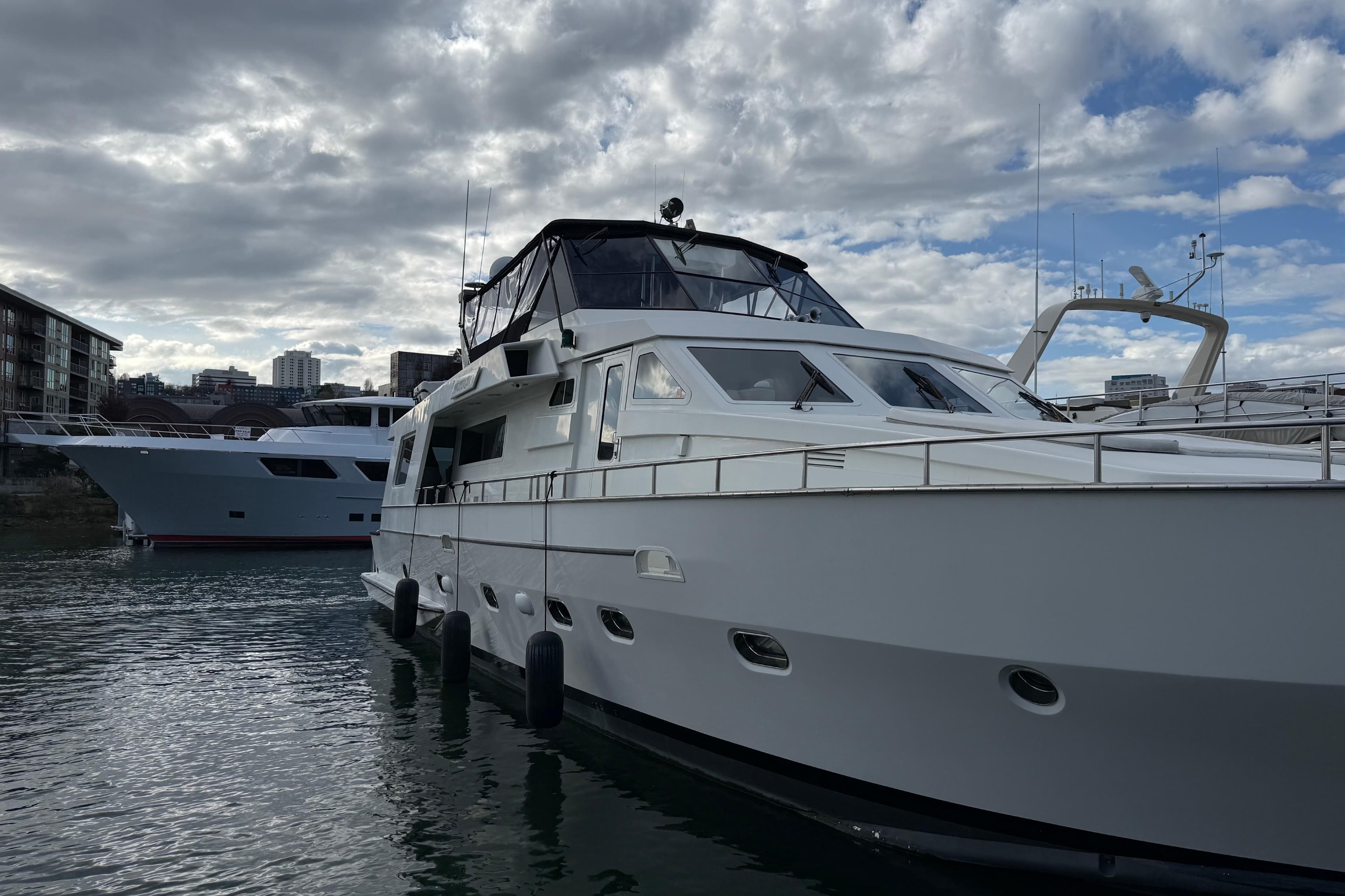 1988 Maiora Motor Yacht docked under cloudy sky, with cityscape in background.