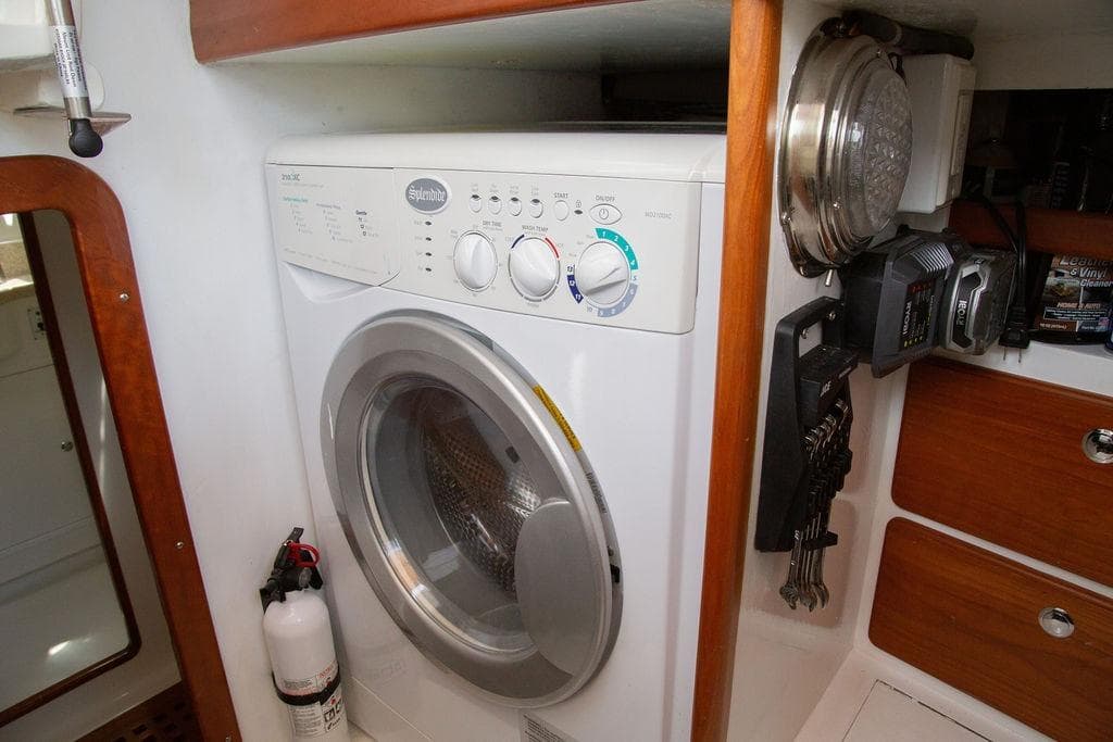 Laundry area inside 2015 Outbound 46 yacht with washer and wooden cabinetry.