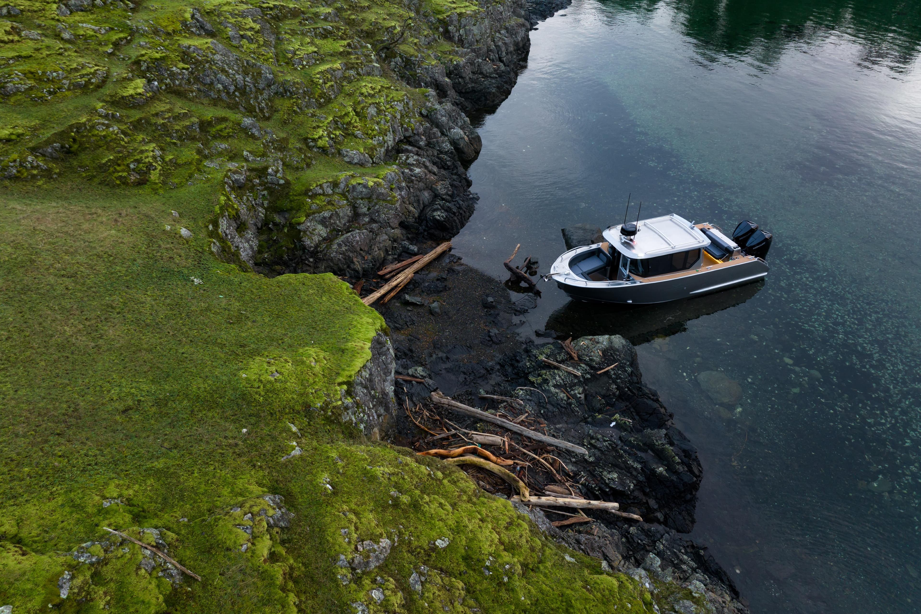 Aerial view of Jasper Marine Defender 22 boat near rocky, moss-covered shoreline, 2026 model.
