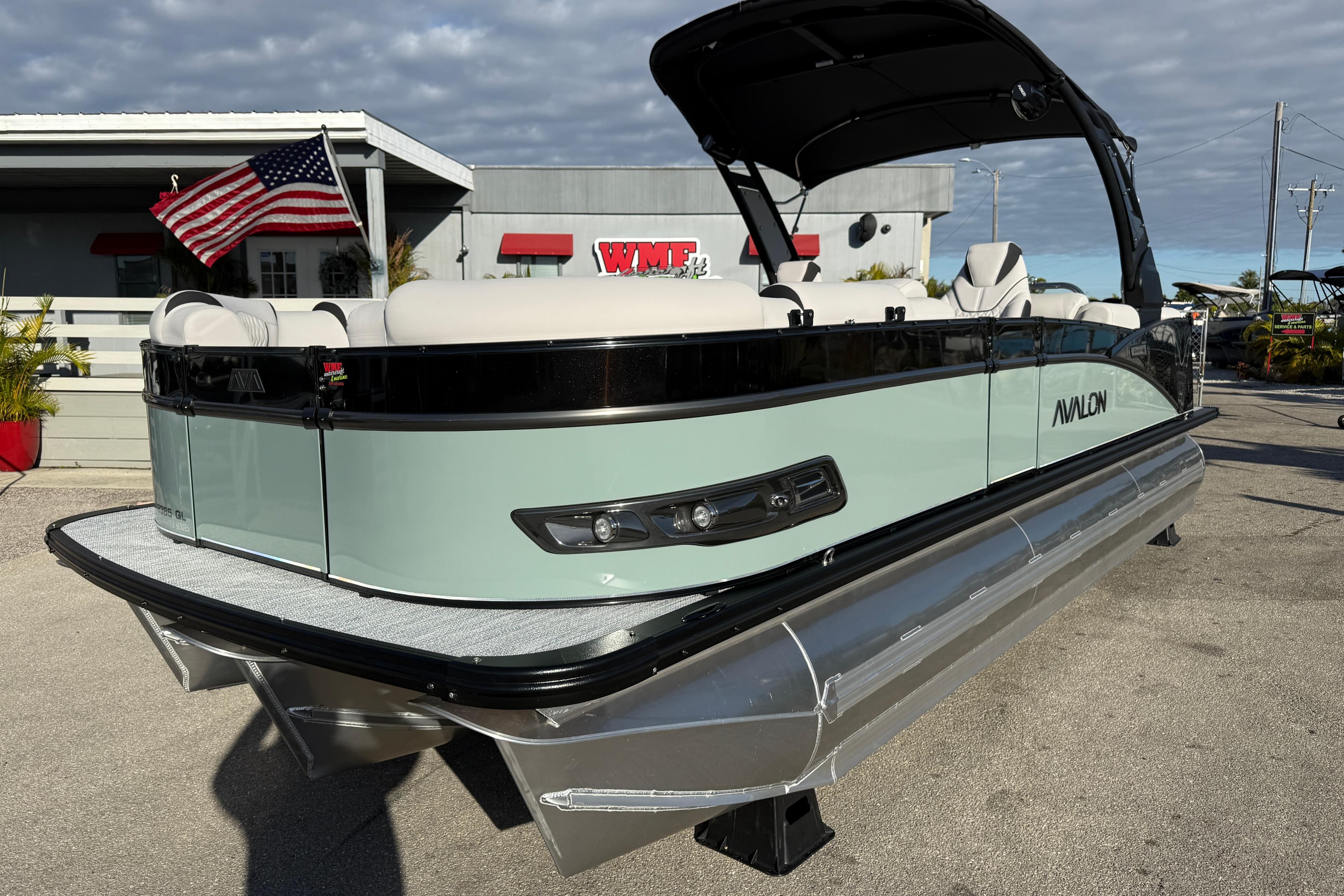 2026 Avalon 2385 Catalina Quad Lounger Tri Toon boat with American flag, parked outdoors.