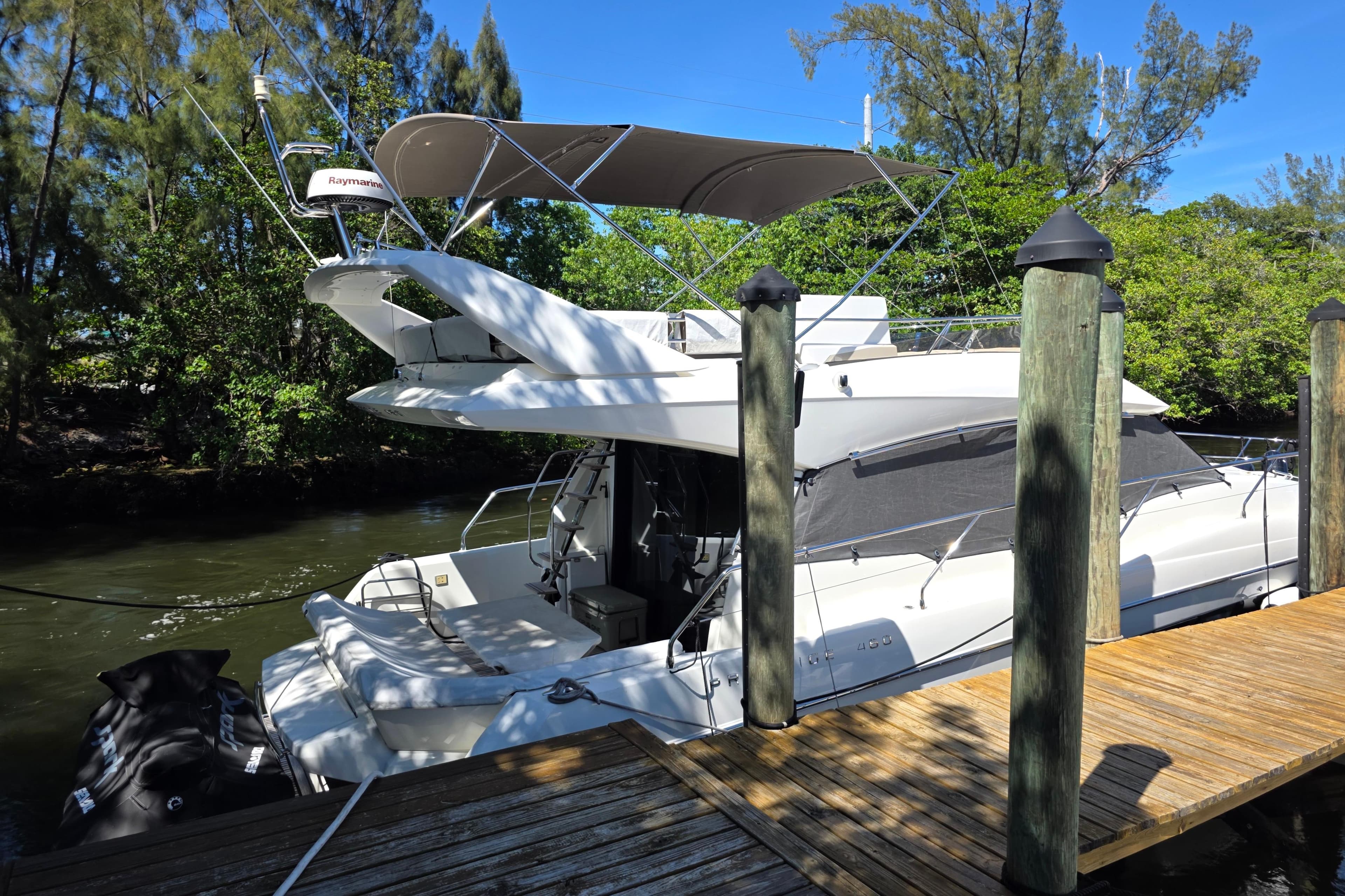 2018 Prestige 460 yacht docked by a wooden pier, surrounded by lush greenery.