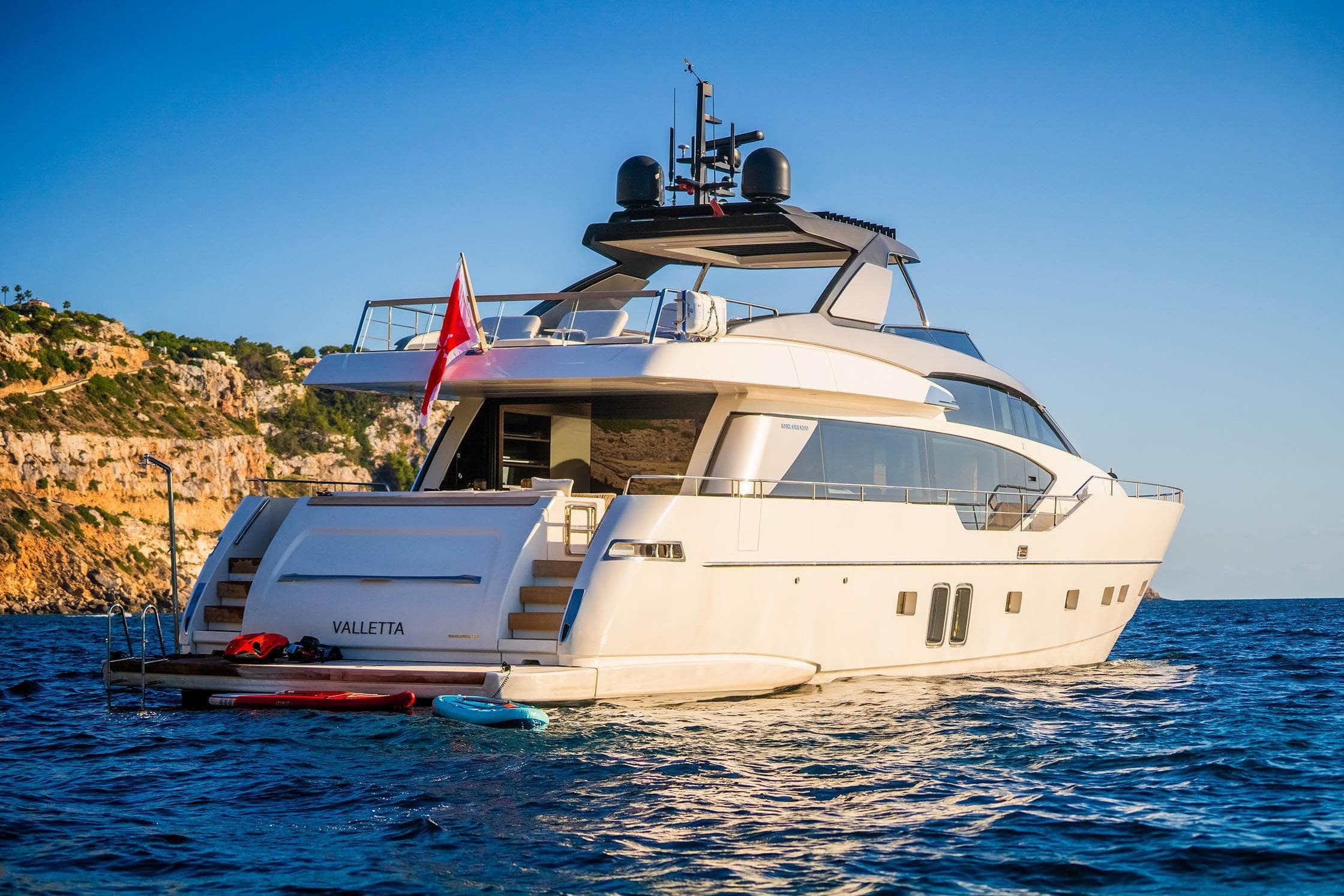 2024 Sanlorenzo SL86 yacht on serene blue waters near rocky coastline.