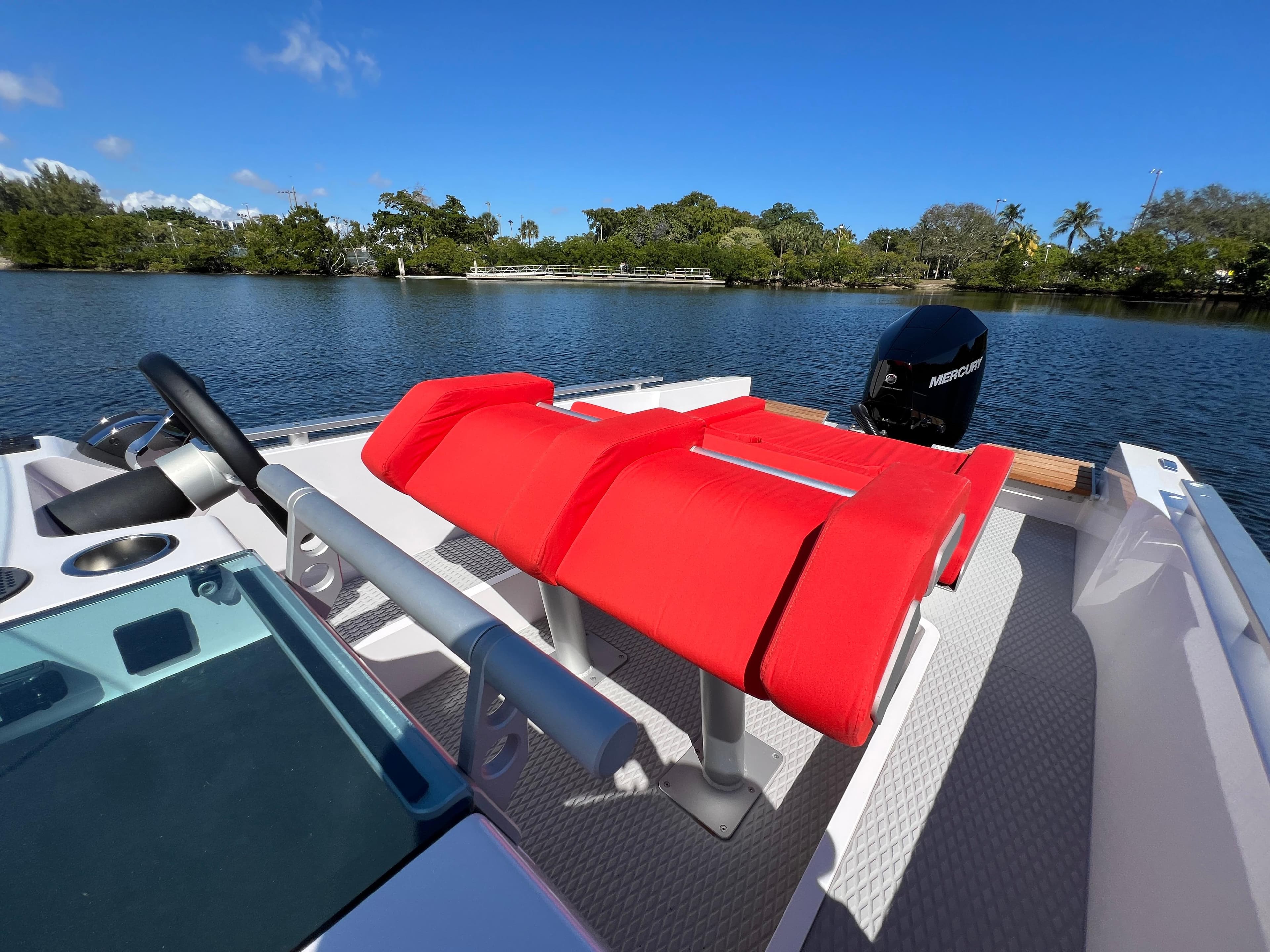2021 Goldfish 23 Tender boat with red seating, steering wheel, and outboard motor on a calm lake.