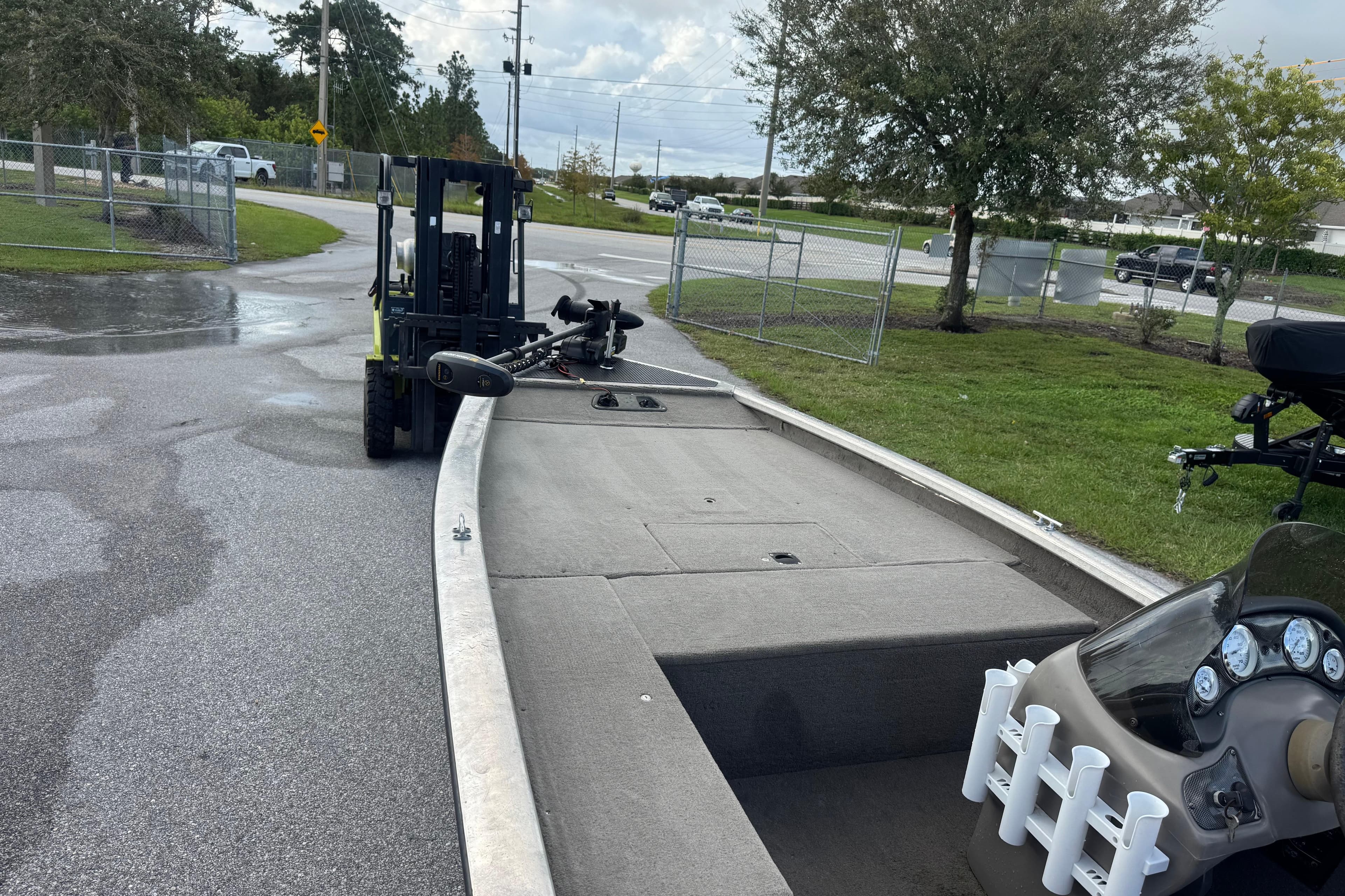 Forklift moving a 2020 Tracker boat on a wet pavement near a fenced area.