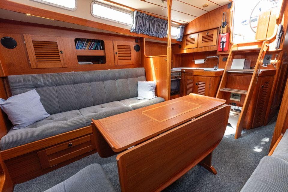Interior of 1997 Hallberg-Rassy 42 yacht with wooden furnishings and cozy seating area.