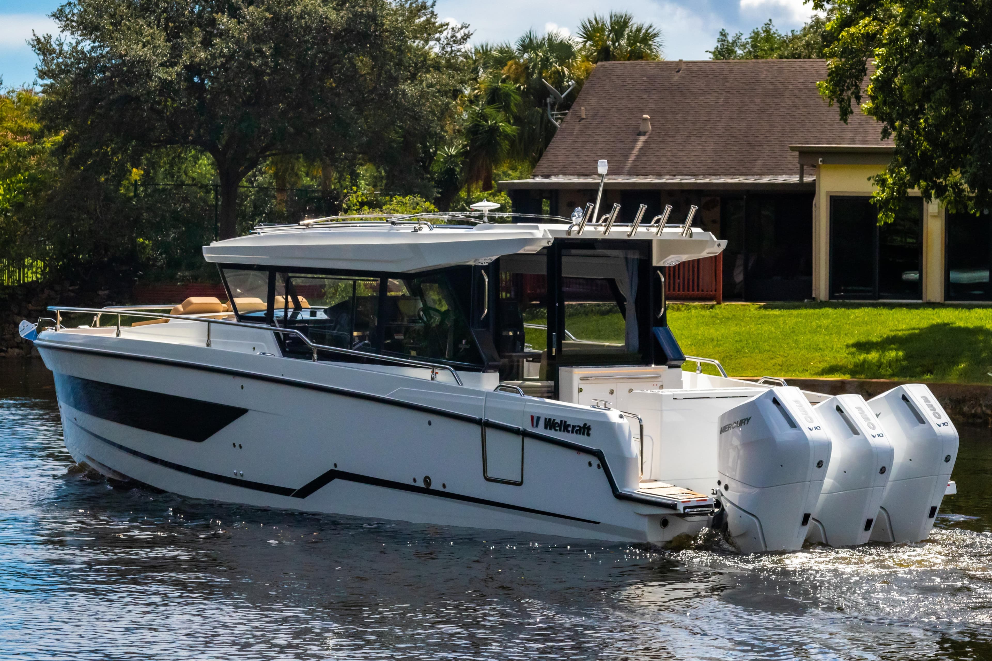 2025 Wellcraft 38 Explorer boat cruising on a sunny day near a house.