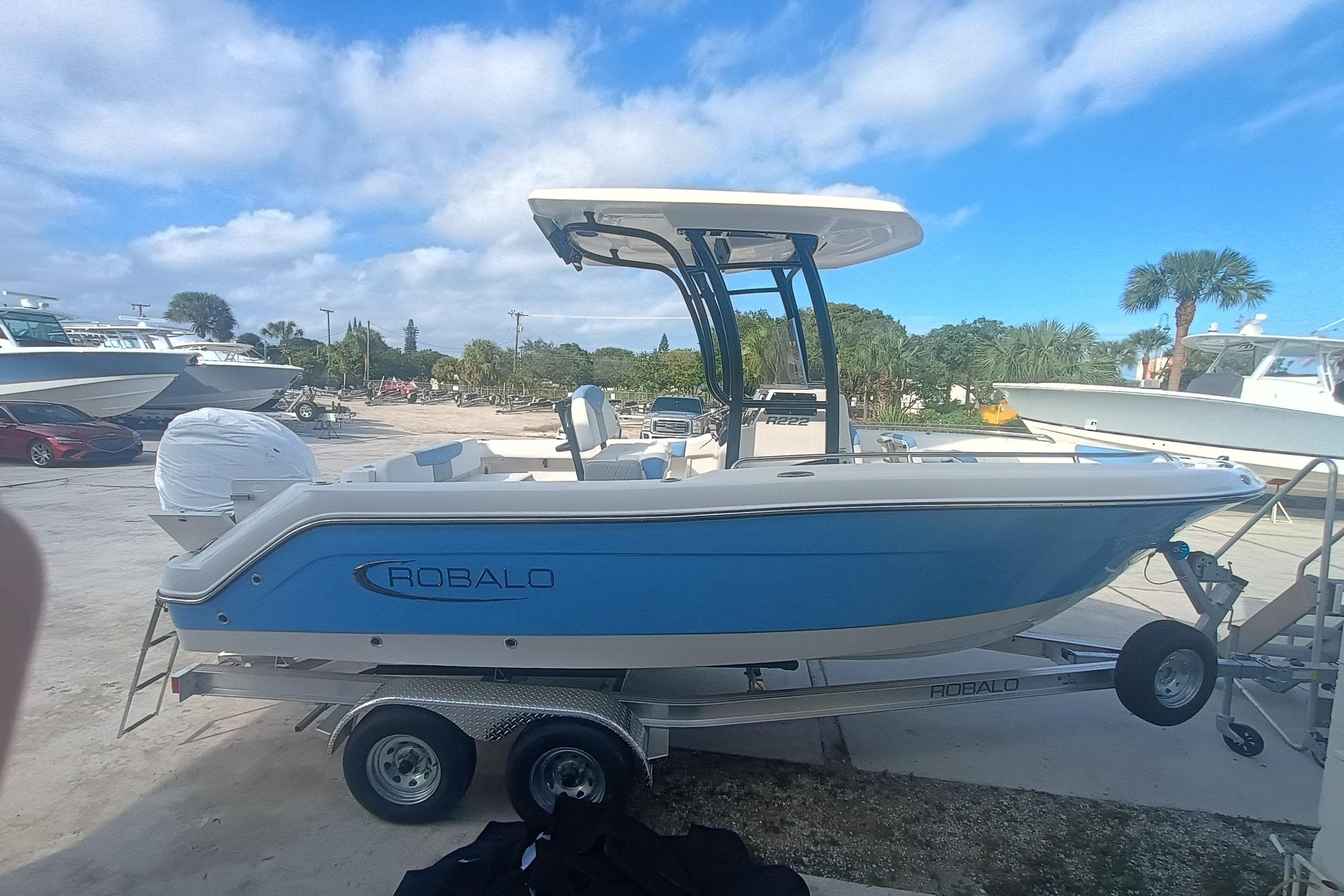 2026 Robalo R222 Explorer boat on trailer, blue hull, parked outdoors under a clear sky.