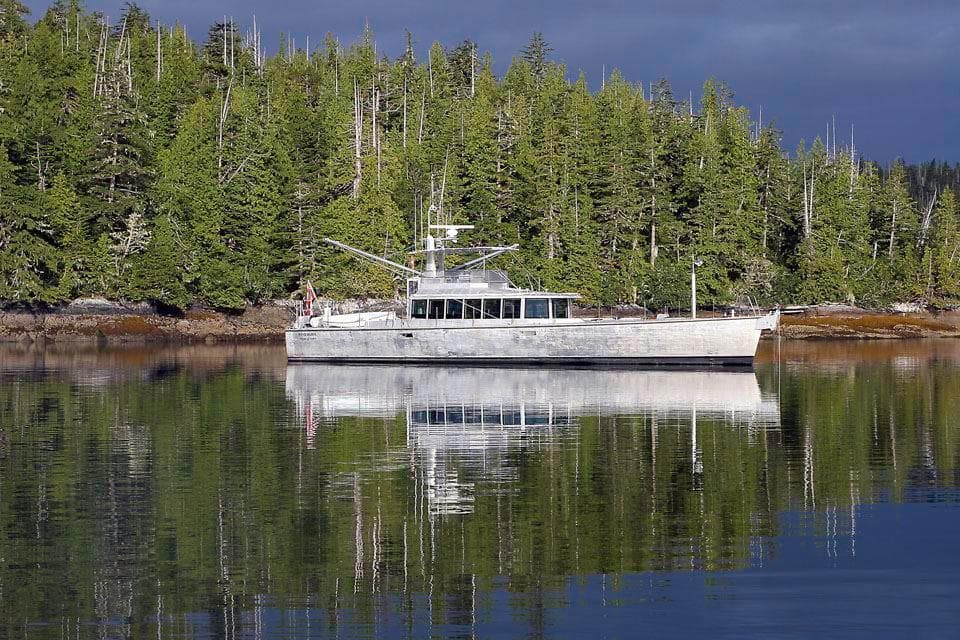Custom FPB 83 yacht from 2005 on calm water, surrounded by lush green forest.