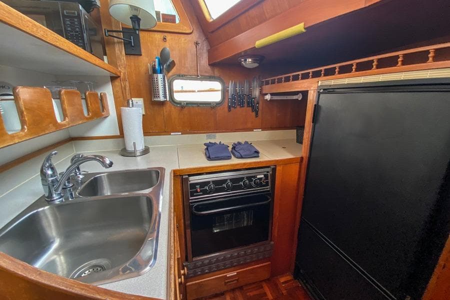 1980 CHB Trawler kitchen with sink, stove, and refrigerator in a wooden interior.