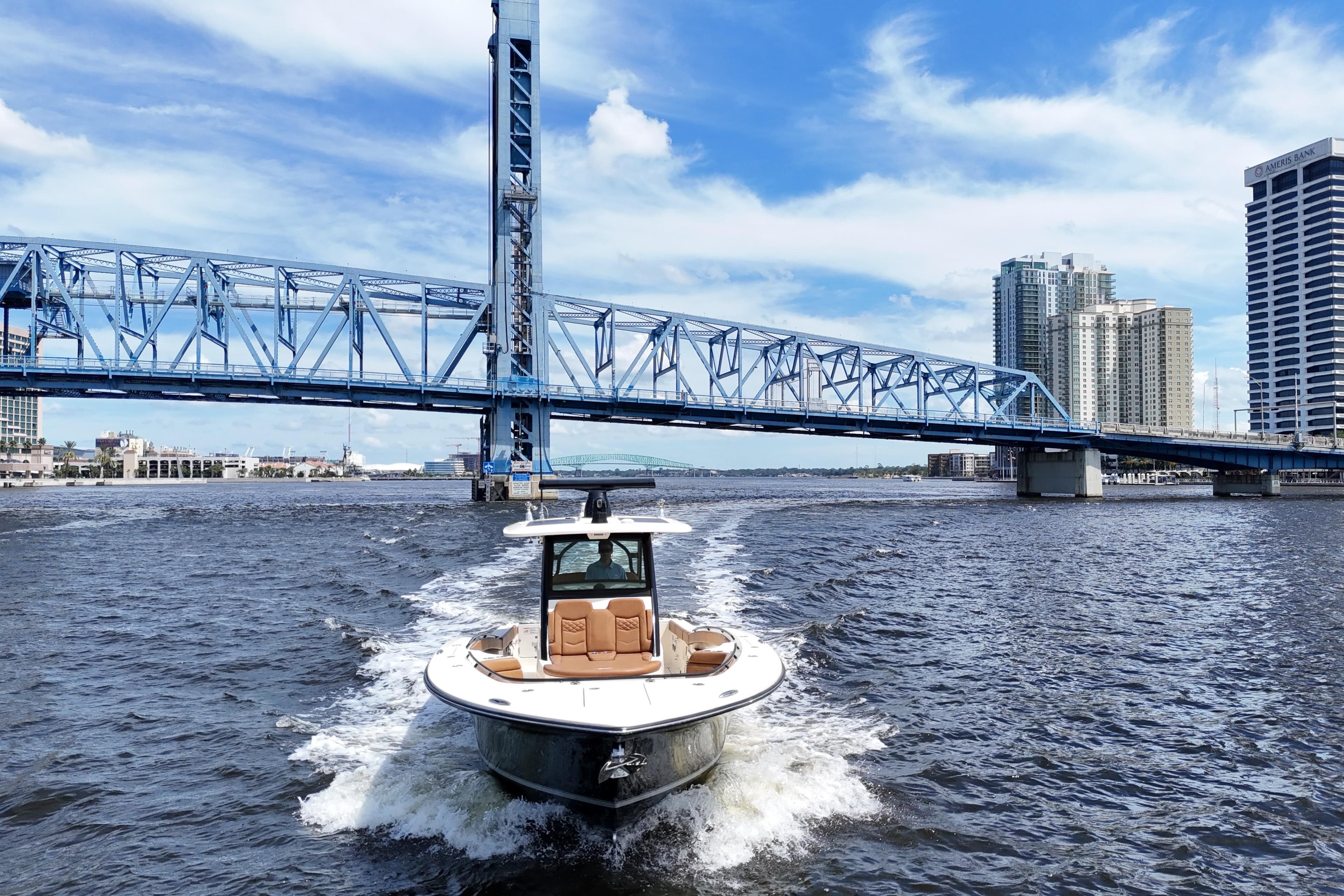 2021 Scout 330 LXF boat cruising under a blue bridge in an urban waterfront setting.