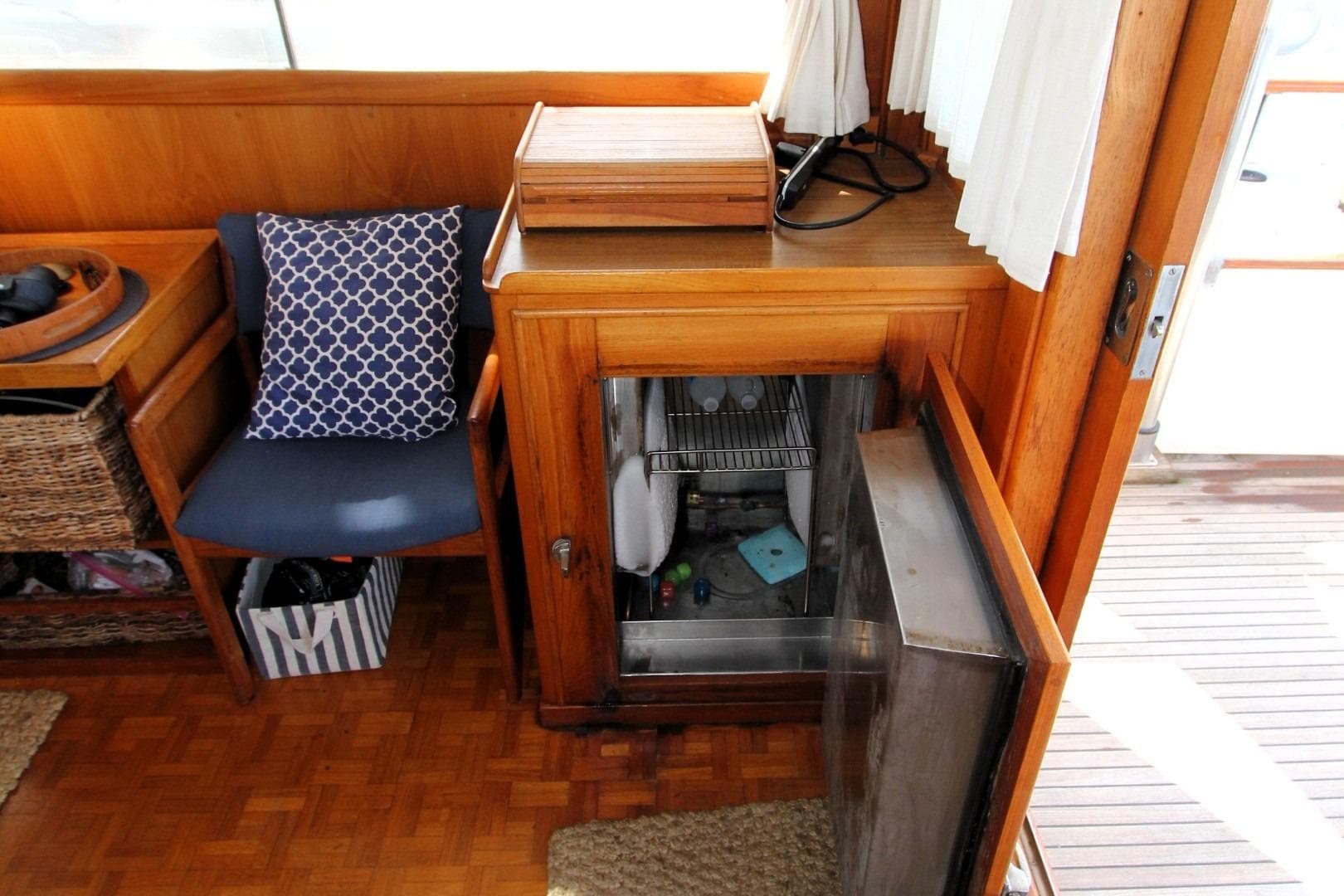 Interior of 1982 Grand Banks 42 Europa with open fridge and blue cushioned chair.