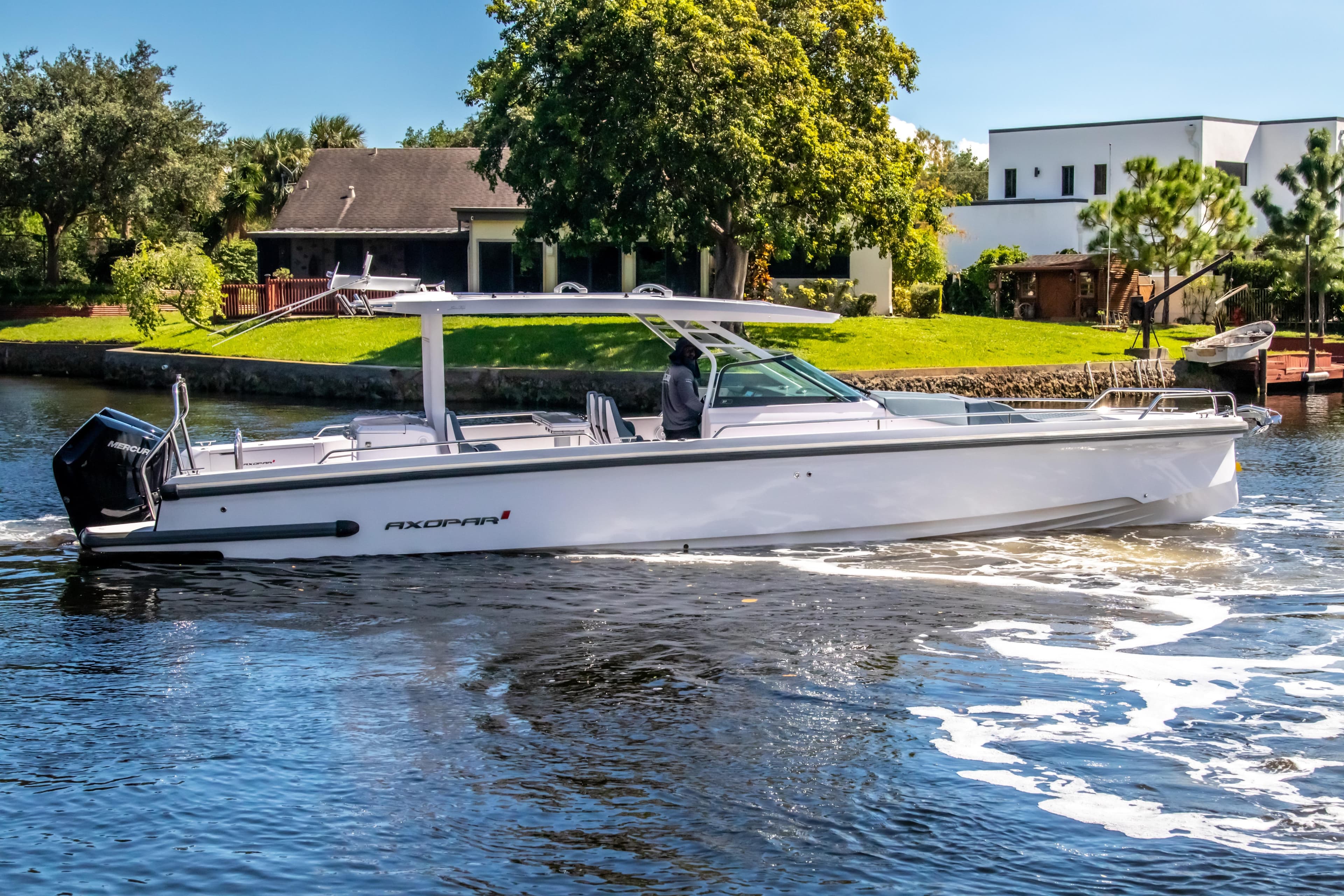 2024 Axopar 37 Sun Top boat cruising on a sunny day near waterfront homes.