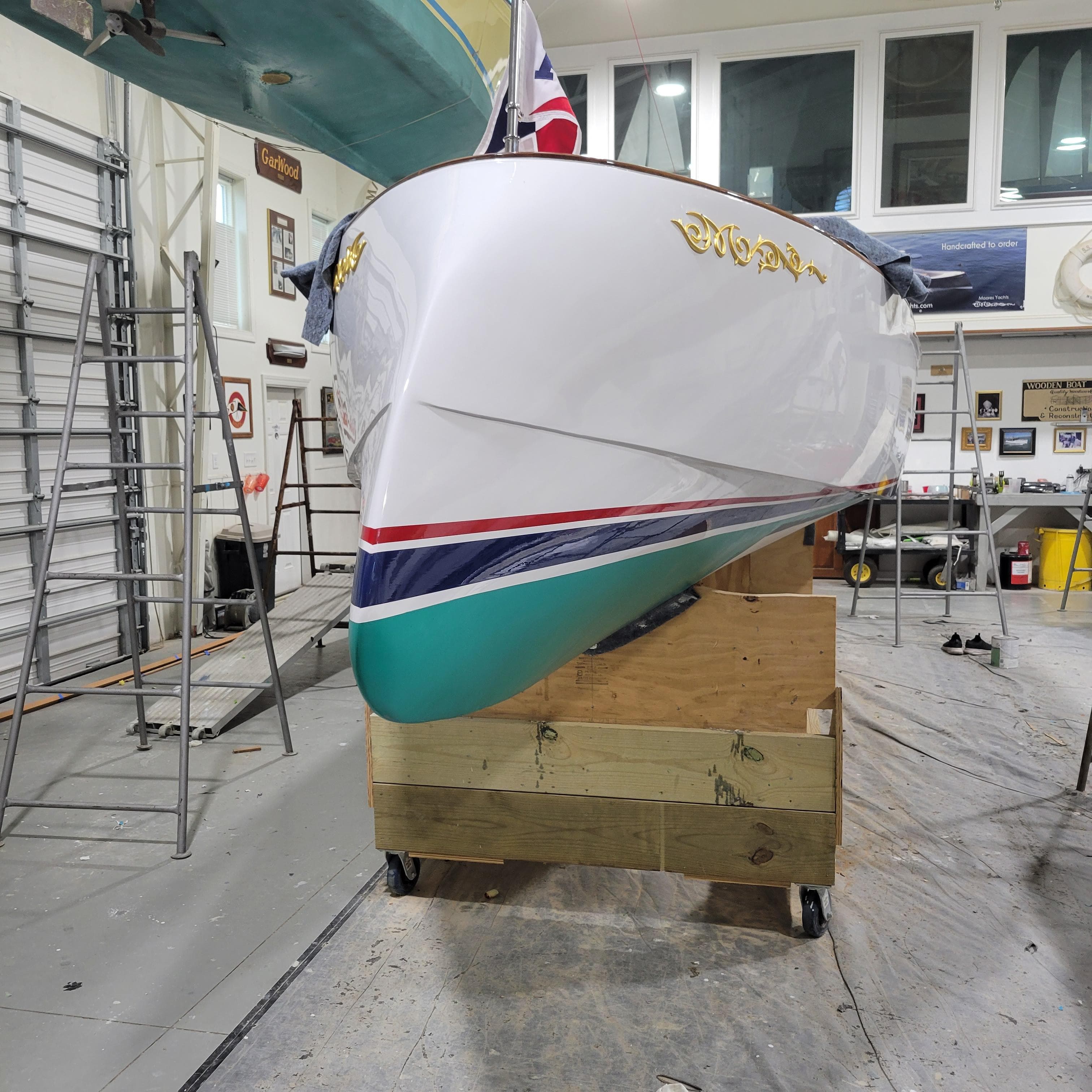 Custom M27 boat in workshop, 2023 model, with vibrant hull colors and gold lettering.