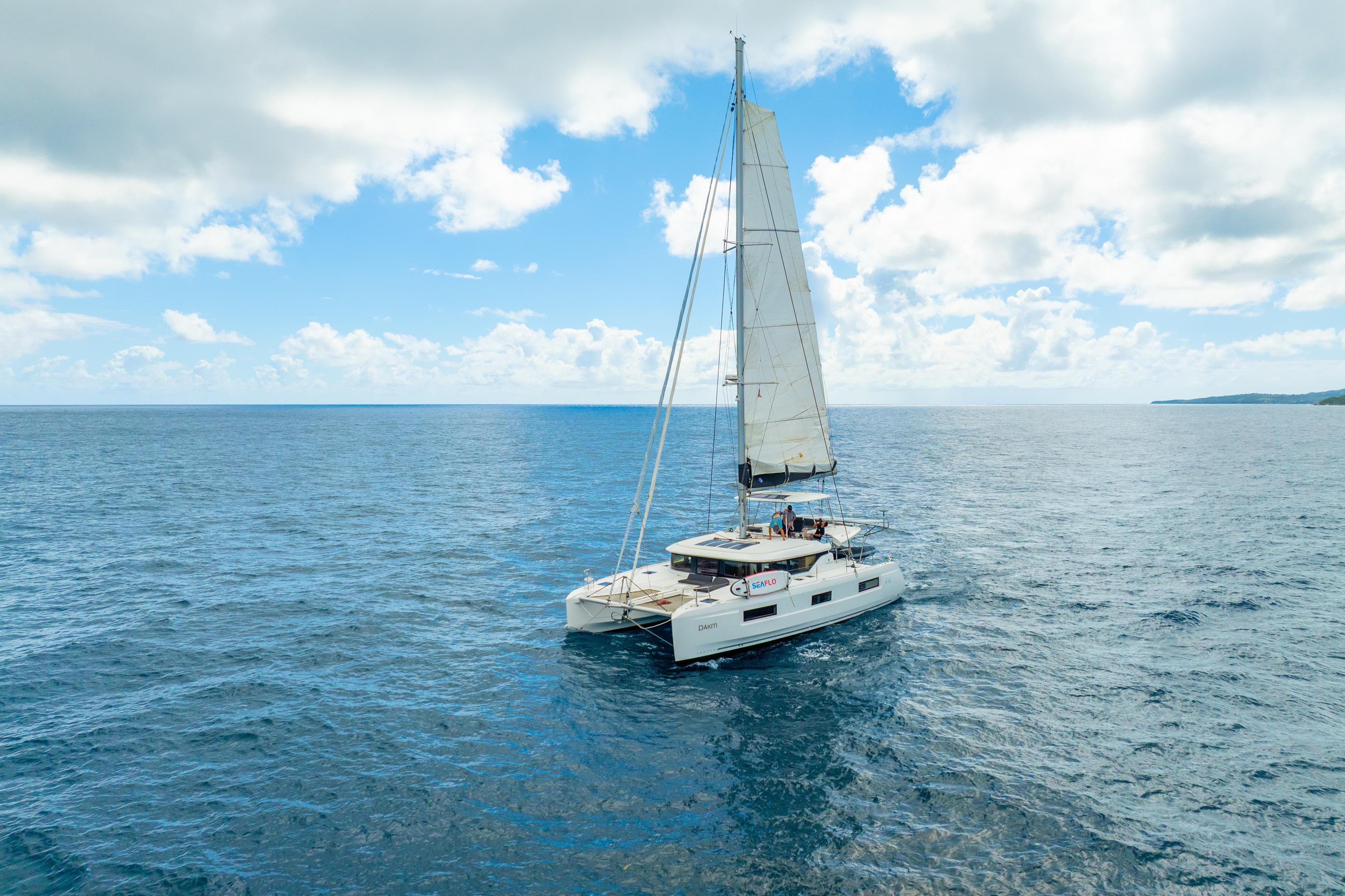 2023 Lagoon 46 catamaran sailing on open ocean under a partly cloudy sky.
