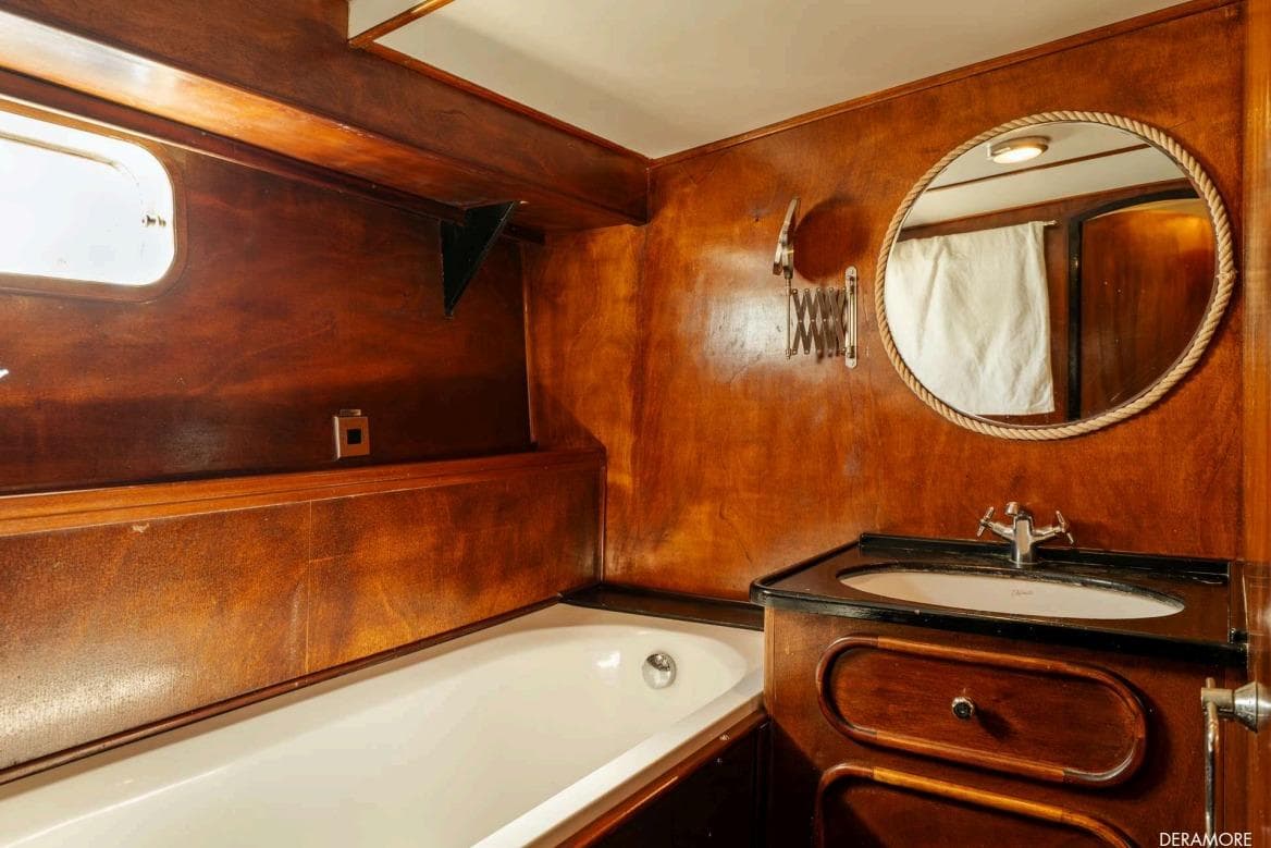 Luxurious wooden bathroom interior on 1971 Dagless Ambassador yacht, featuring bathtub and round mirror.