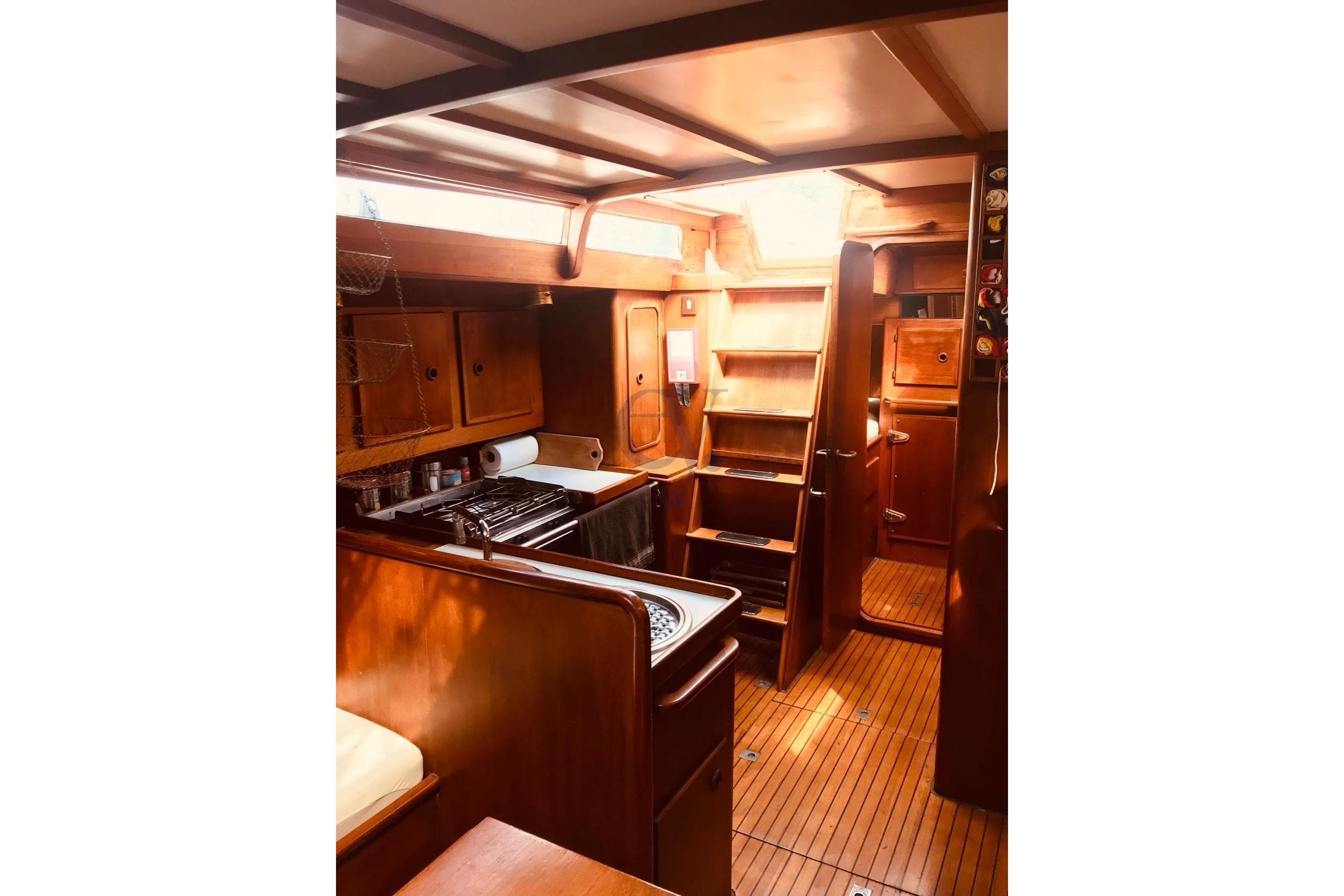 Interior of a 1975 Sciarelli 47 sailboat with wooden cabinetry and compact kitchen.