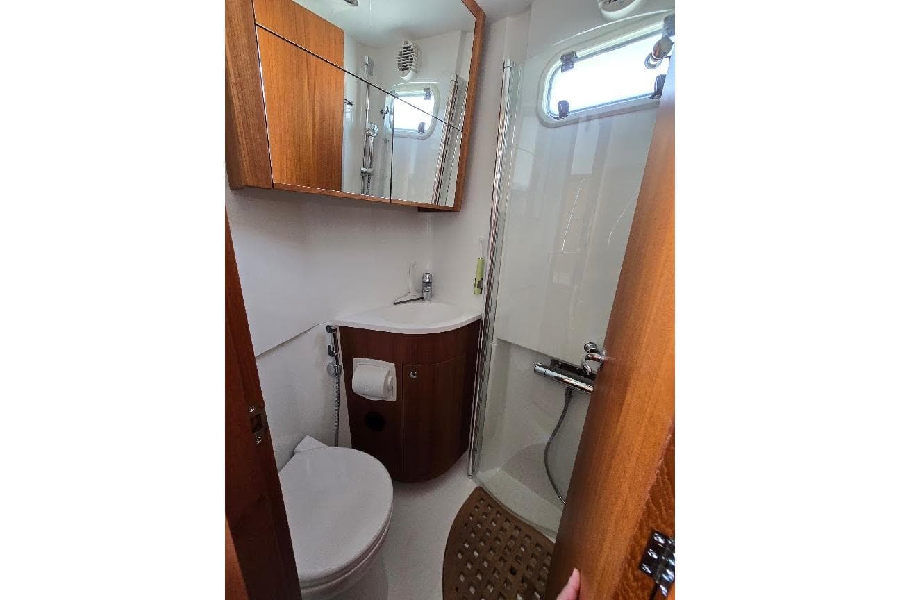 Compact bathroom in 2022 Targa 37 boat with shower, sink, and wooden cabinetry.