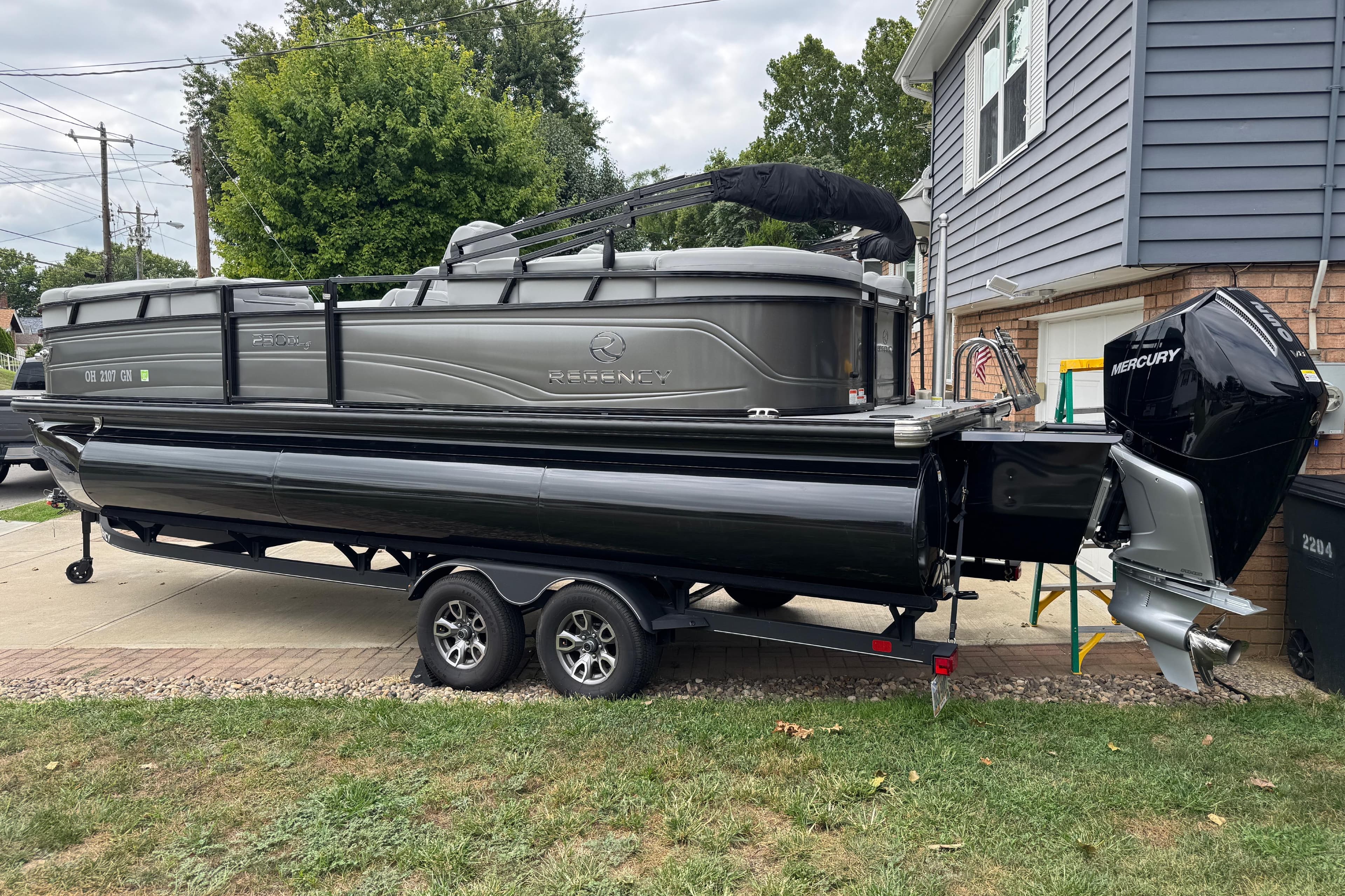 2024 Regency 230 DL3 pontoon boat on trailer, parked in residential driveway.