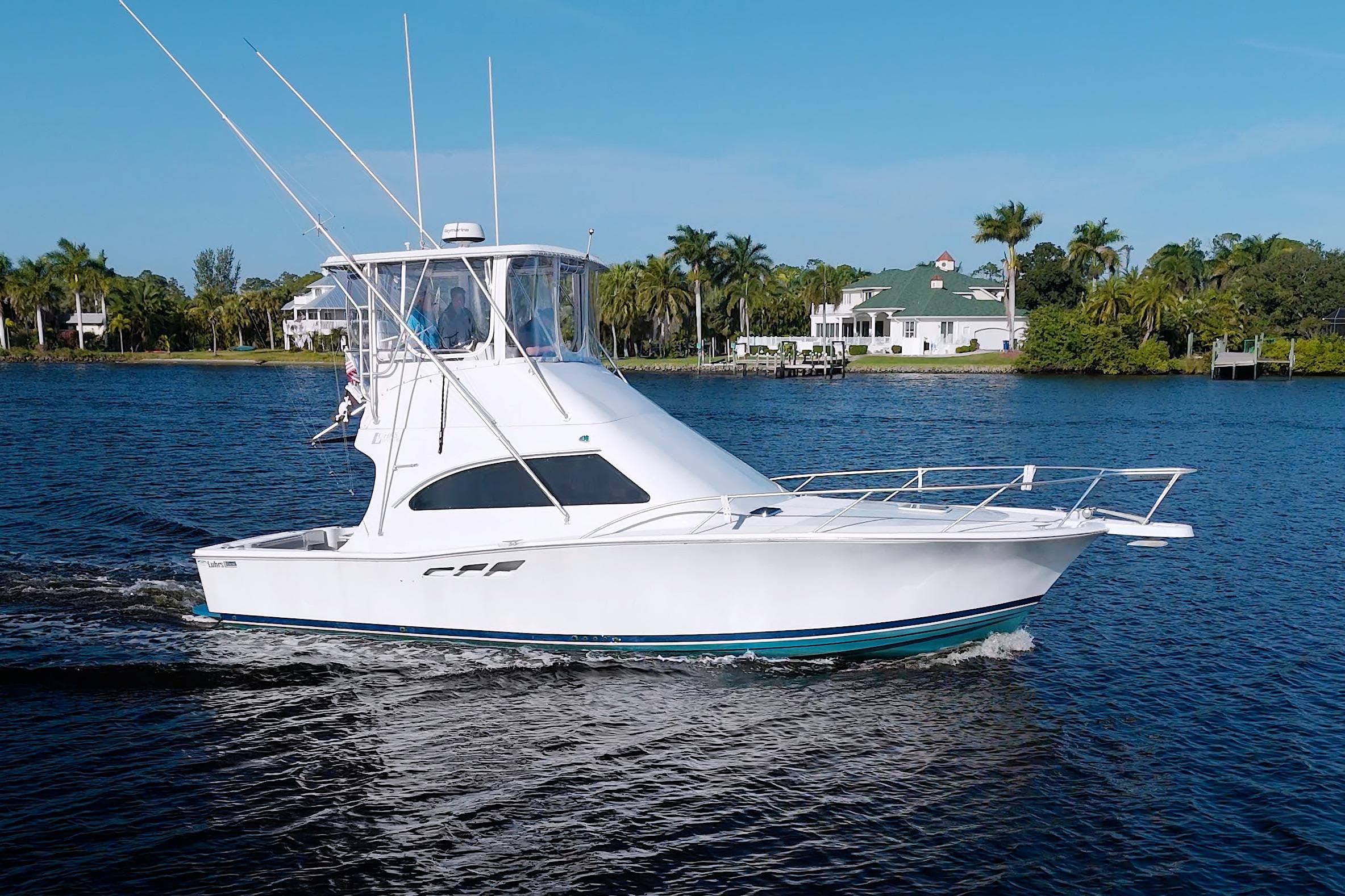 1998 Luhrs 36 Convertible yacht cruising on a scenic waterway with palm trees.