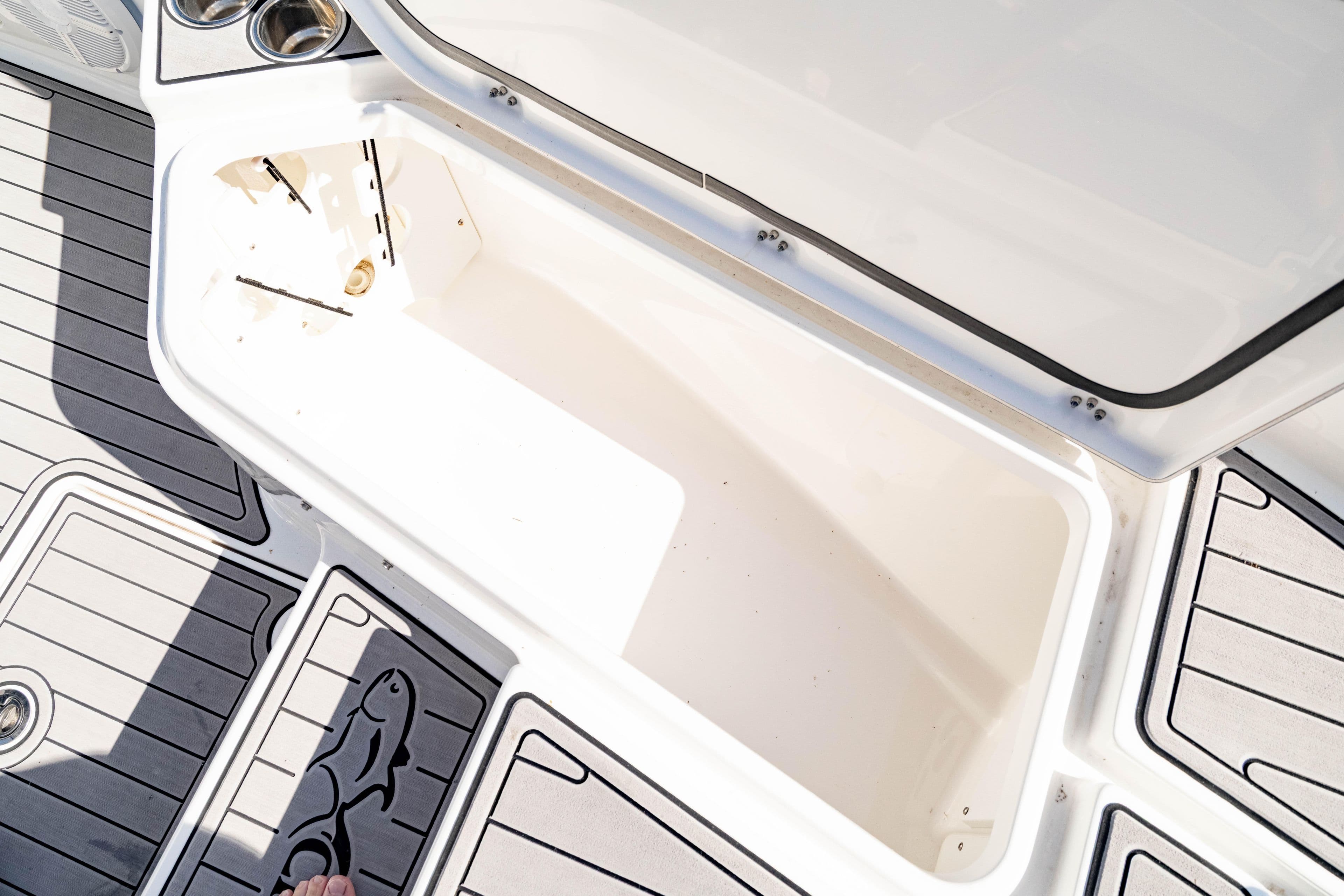 Open storage compartment on 2023 Crevalle 26 HCO boat deck, featuring cup holders and fish design.