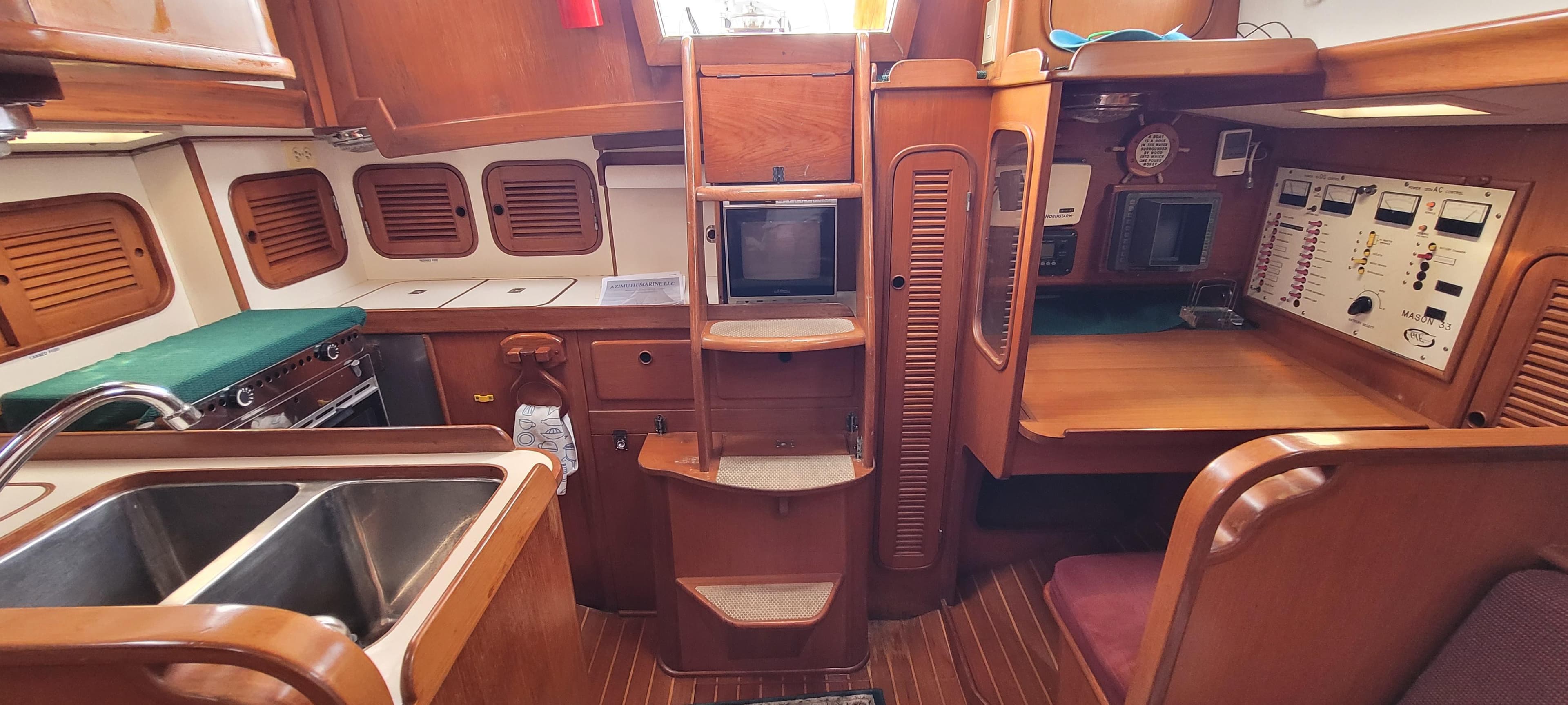 Interior of 1985 Mason 33 Sloop, featuring kitchen, seating, and navigation area.