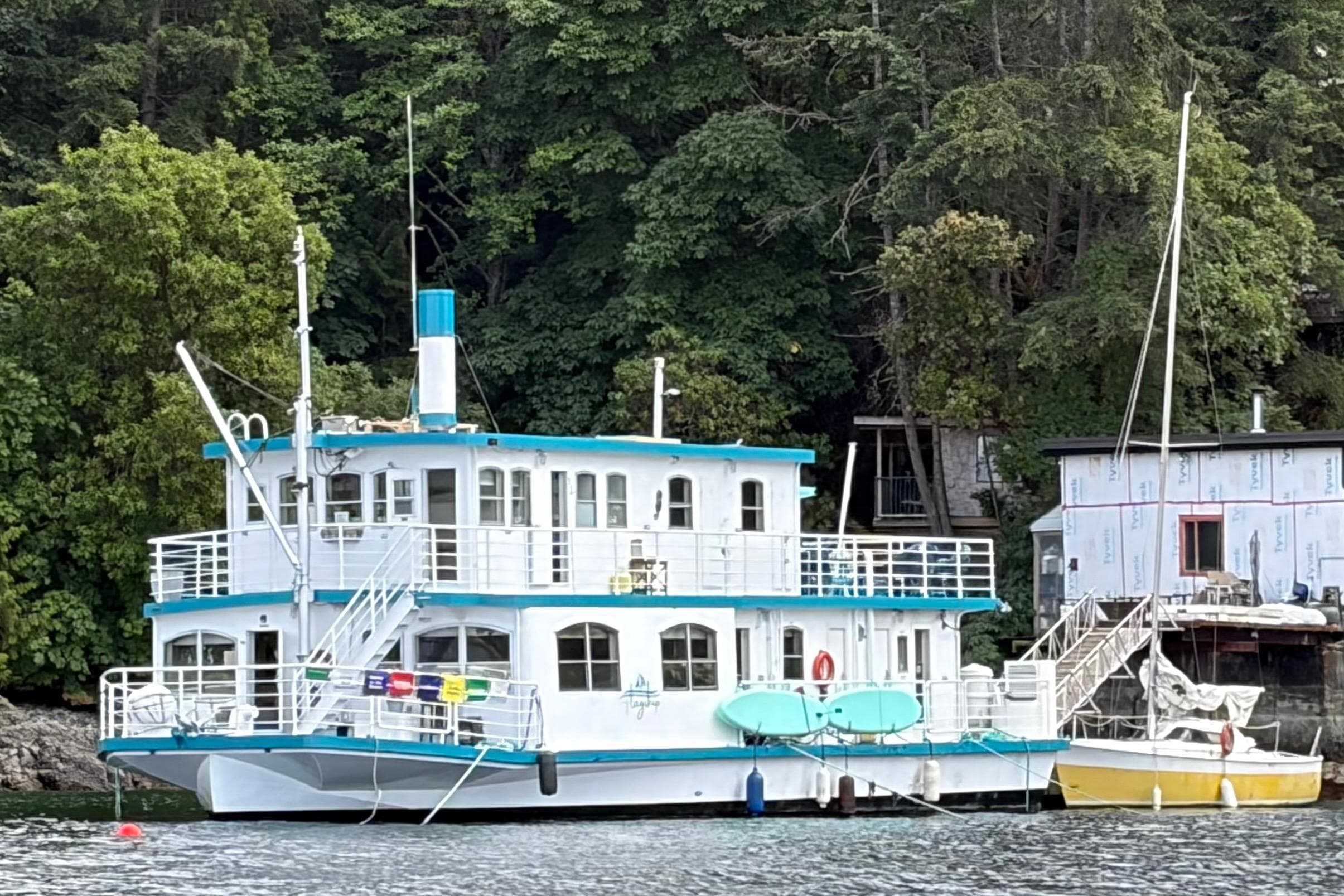 Houseboat conversion, Titan 1988, docked by lush greenery and adjacent structures.
