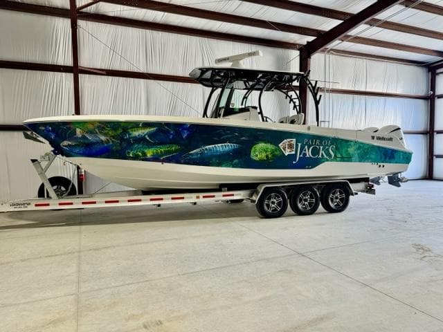 2020 Wellcraft 302 Fisherman boat on trailer in warehouse, Pair of Jacks graphic on side.