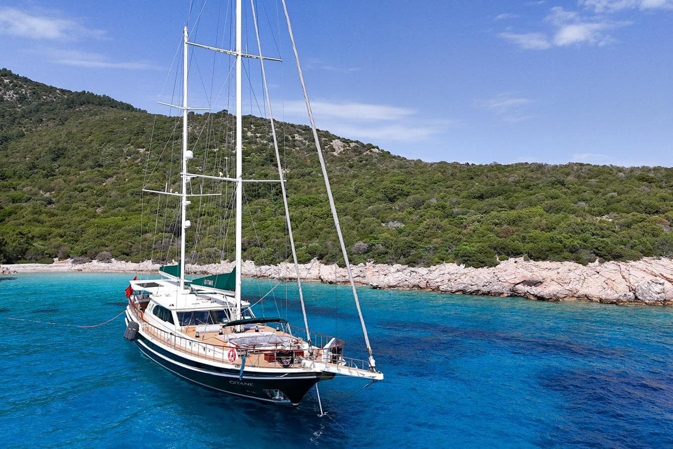 Sailing yacht Evadne 37mt (2008) anchored in clear blue waters near a lush coastline.