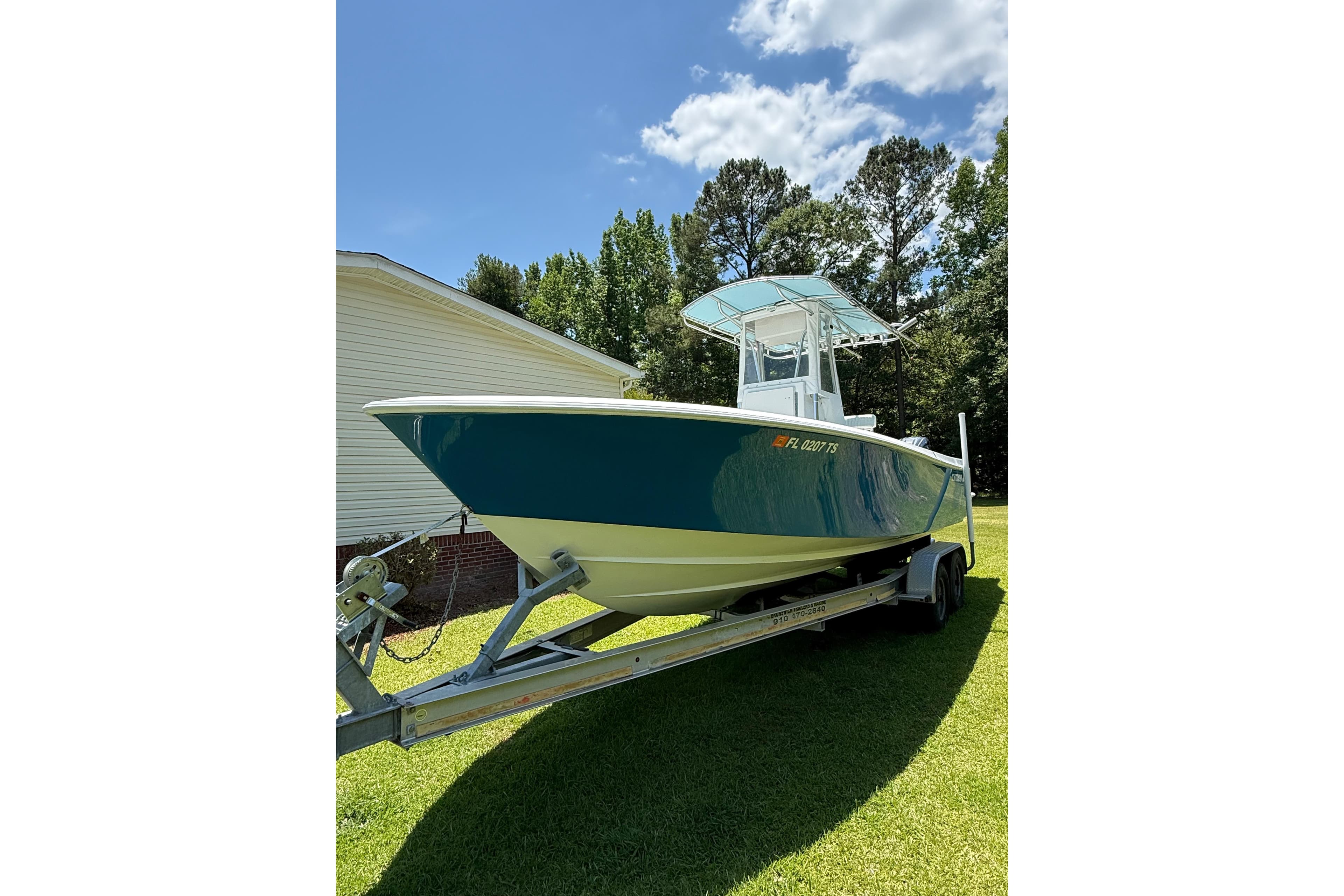 2015 Contender 25 Tournament boat on trailer, parked on grass under blue sky.