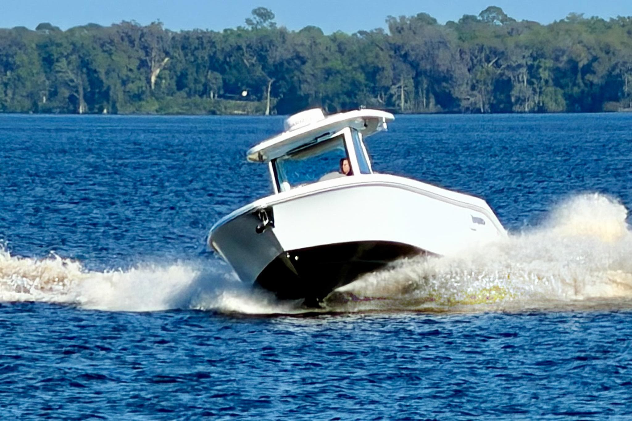 2025 Everglades 315 Center Console boat cruising on a lake with forested background.