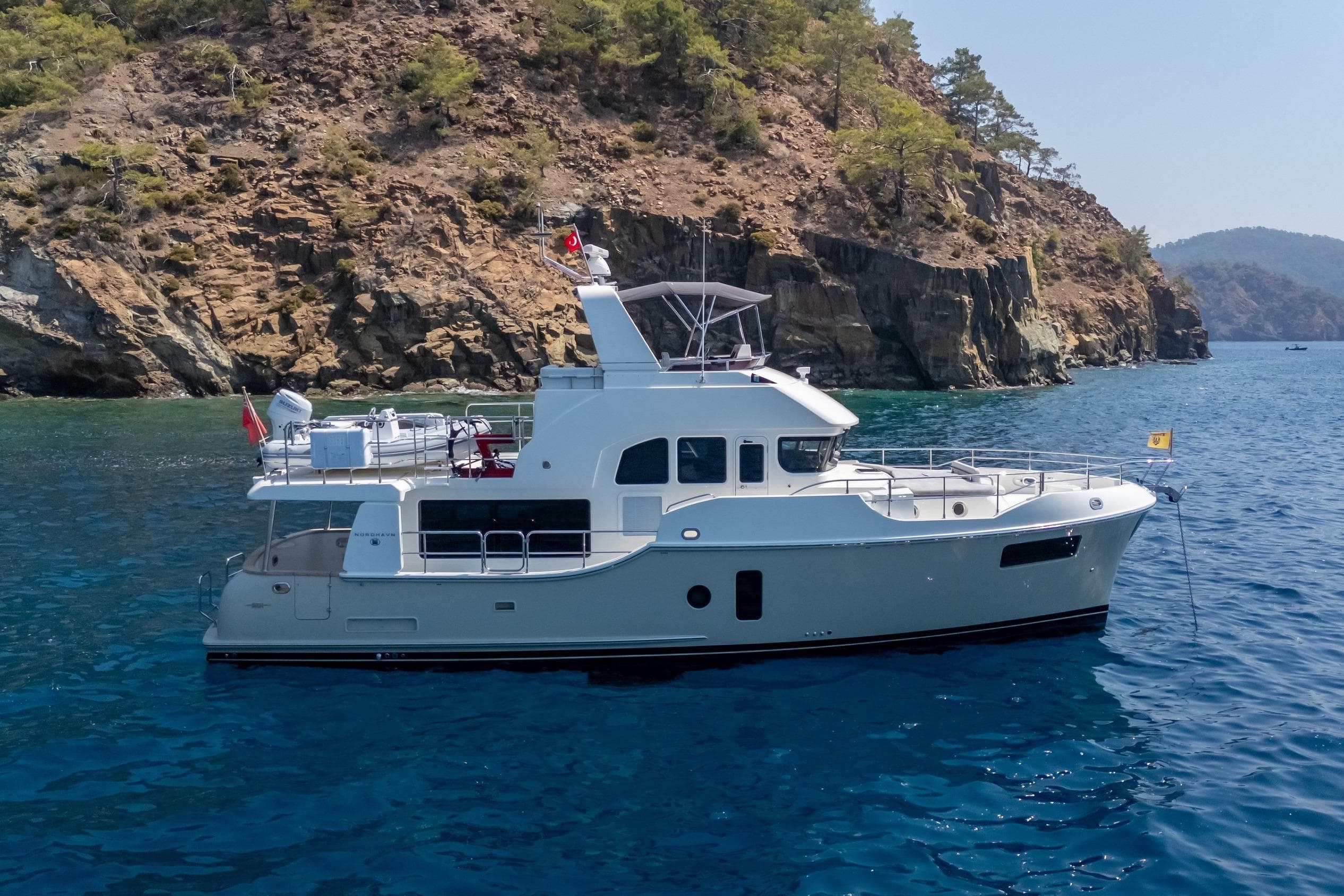 2024 Nordhavn 51 yacht anchored near rocky coastline in clear blue water.