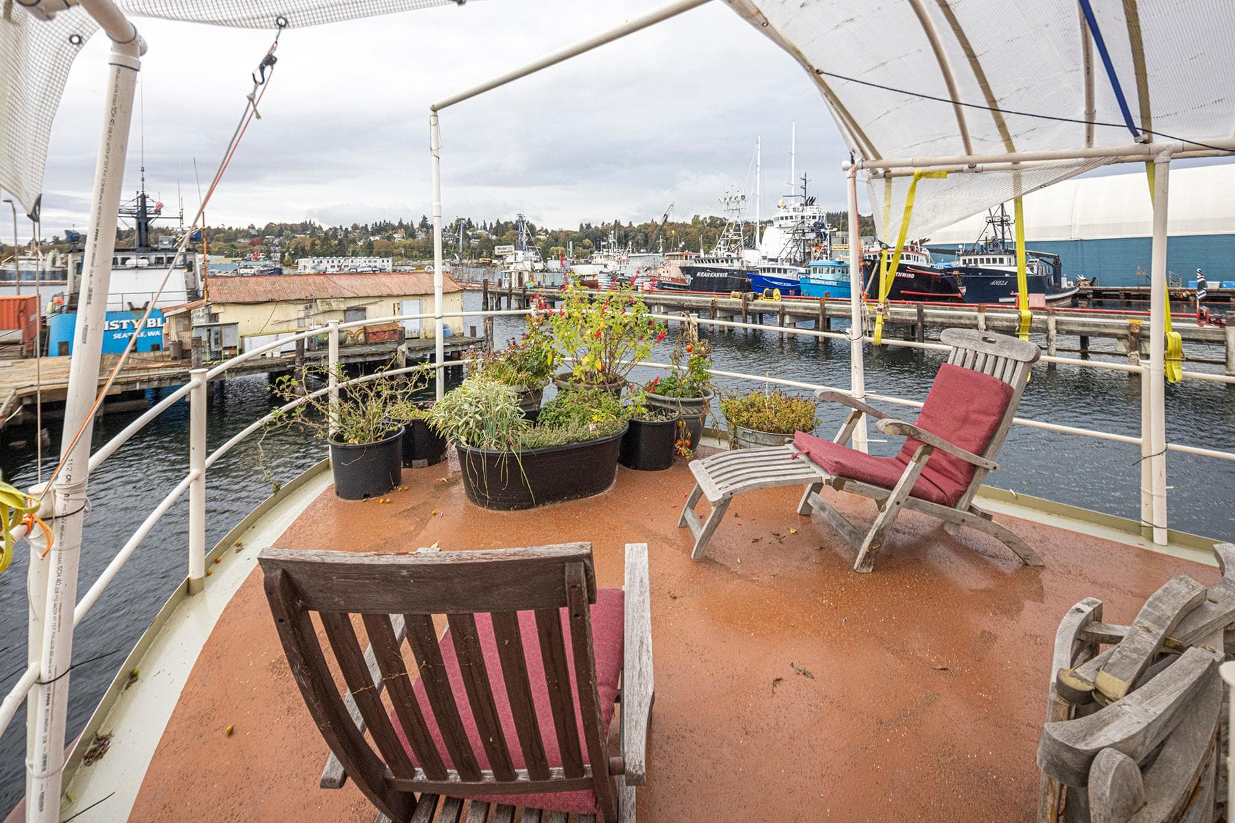 Deck of 1943 Custom Navy Tug with chairs and potted plants, overlooking a marina.