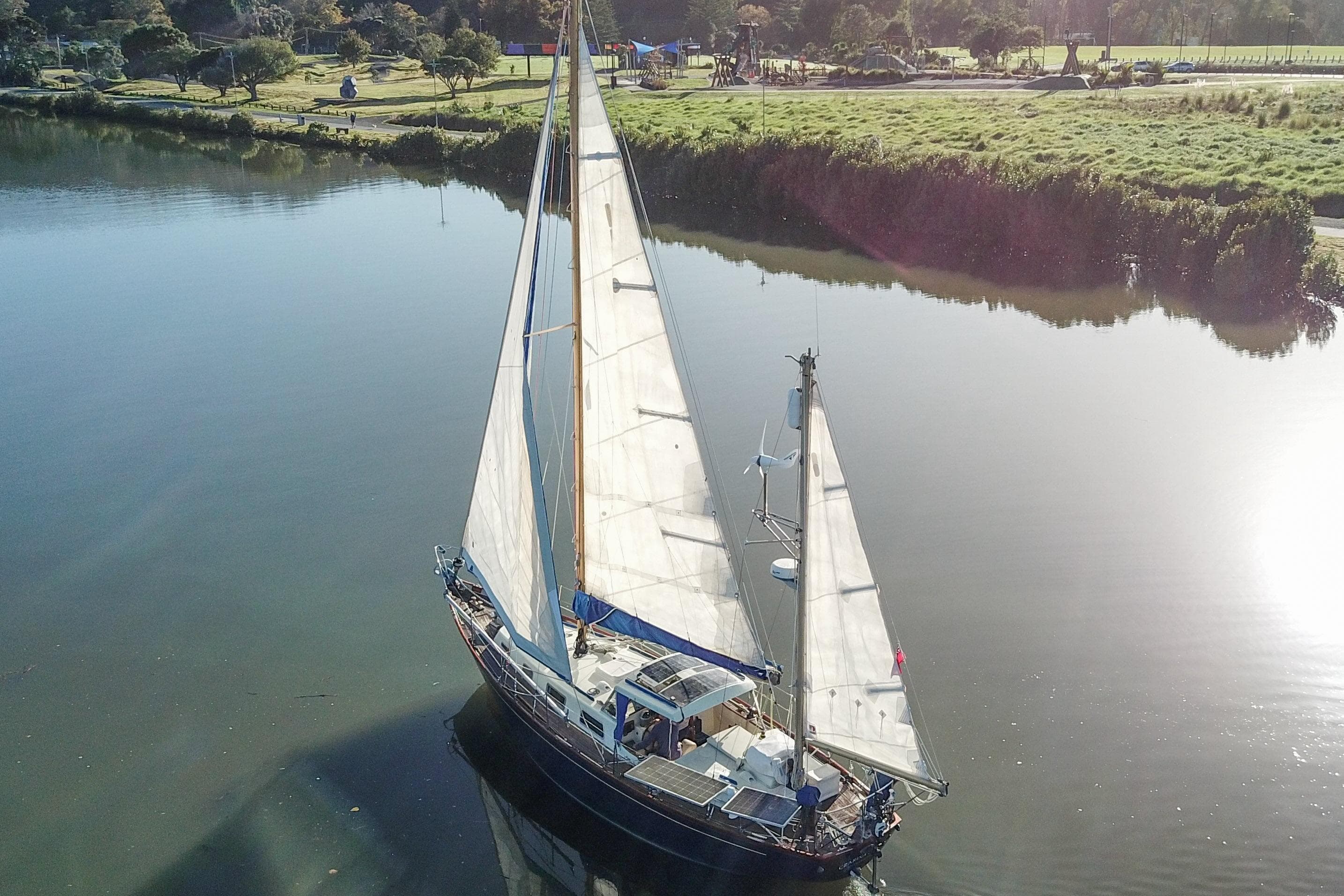 Vintage 1973 Camper & Nicholsons 38 sailboat on calm river, surrounded by lush greenery.