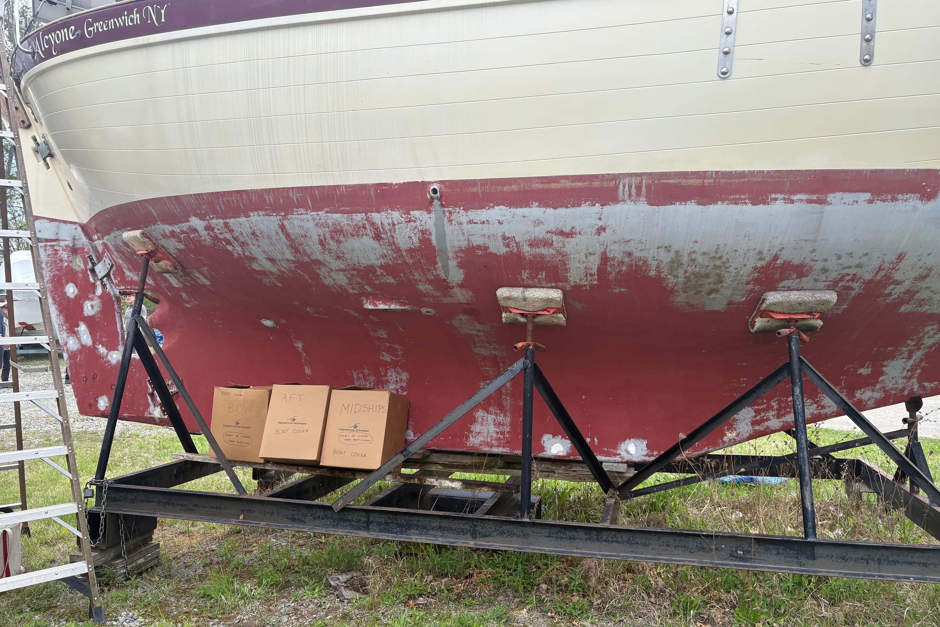 1978 Pacific Seacraft 31 sailboat on stands, hull showing wear, with labeled boxes nearby.