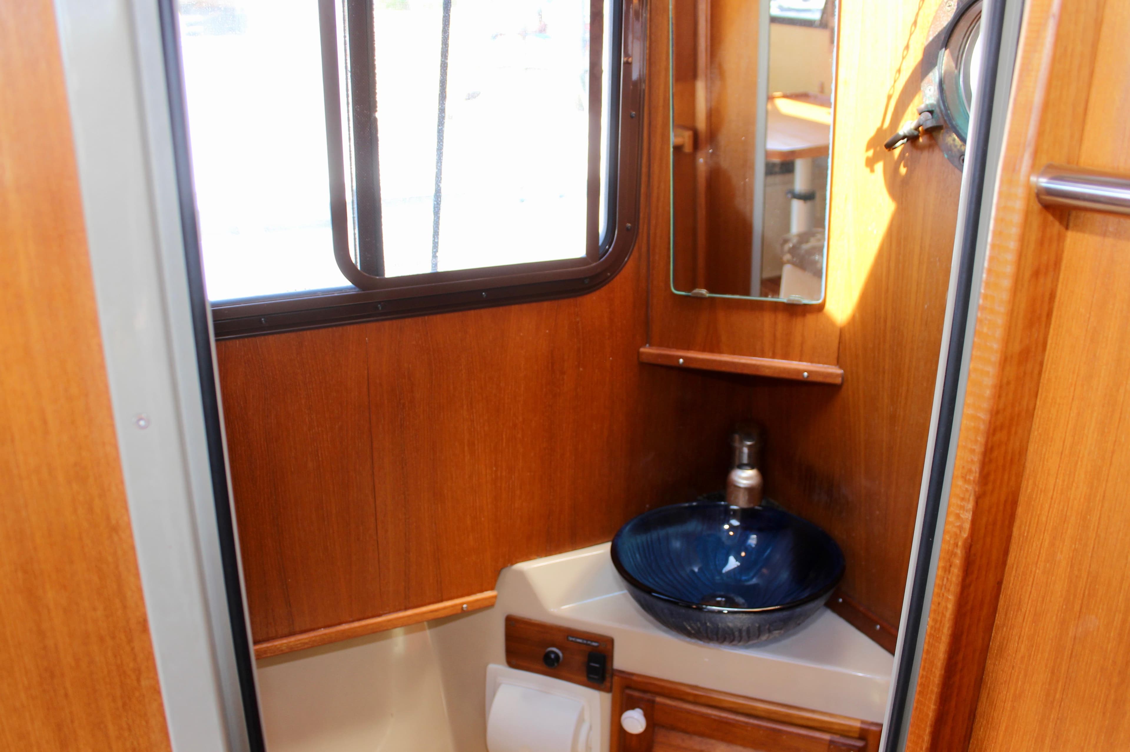 Compact bathroom interior of 2011 Ranger Tugs R-27 with wooden finish and blue sink.