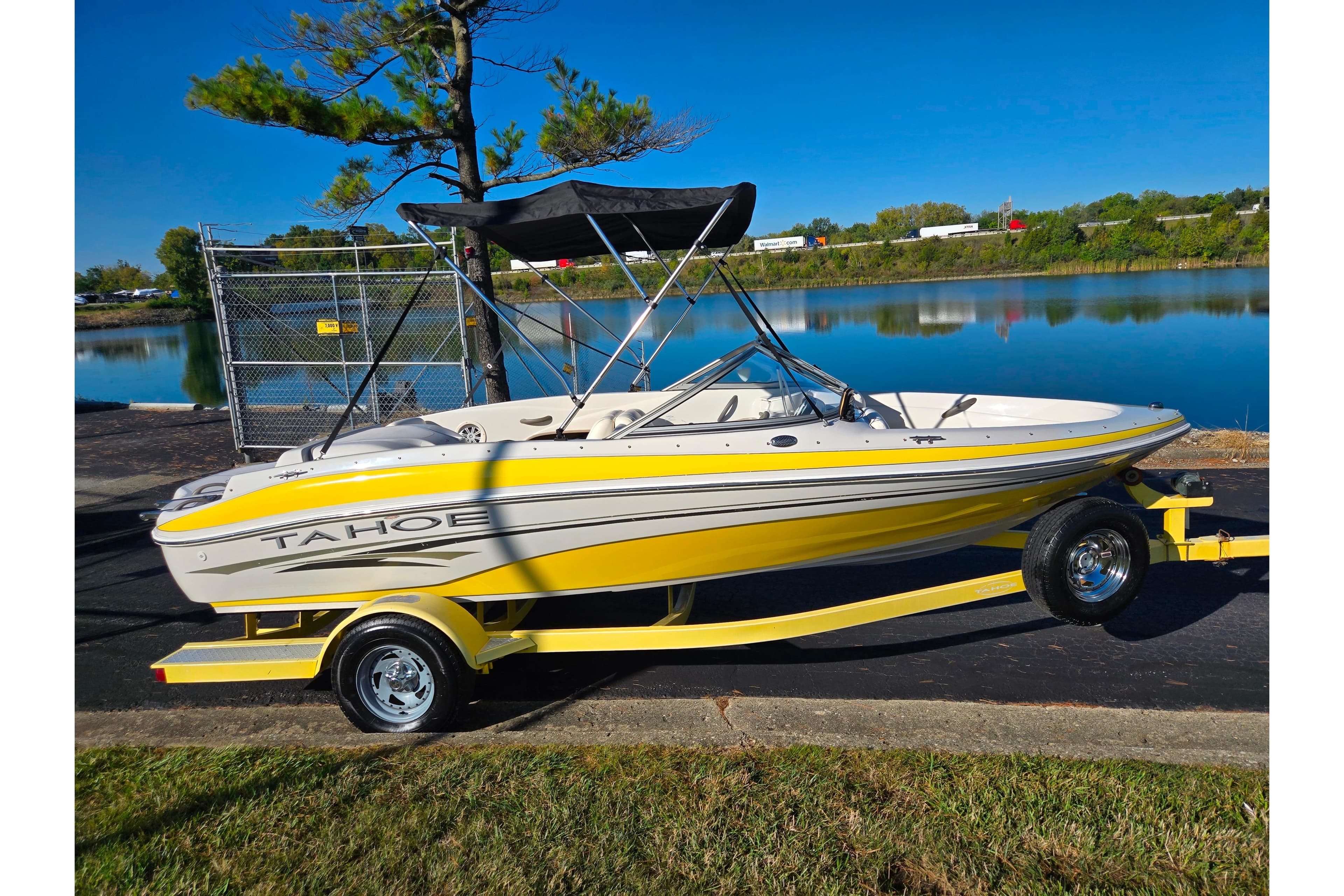 2006 Tahoe Q4 Sport boat on trailer by a serene lake under clear blue sky.
