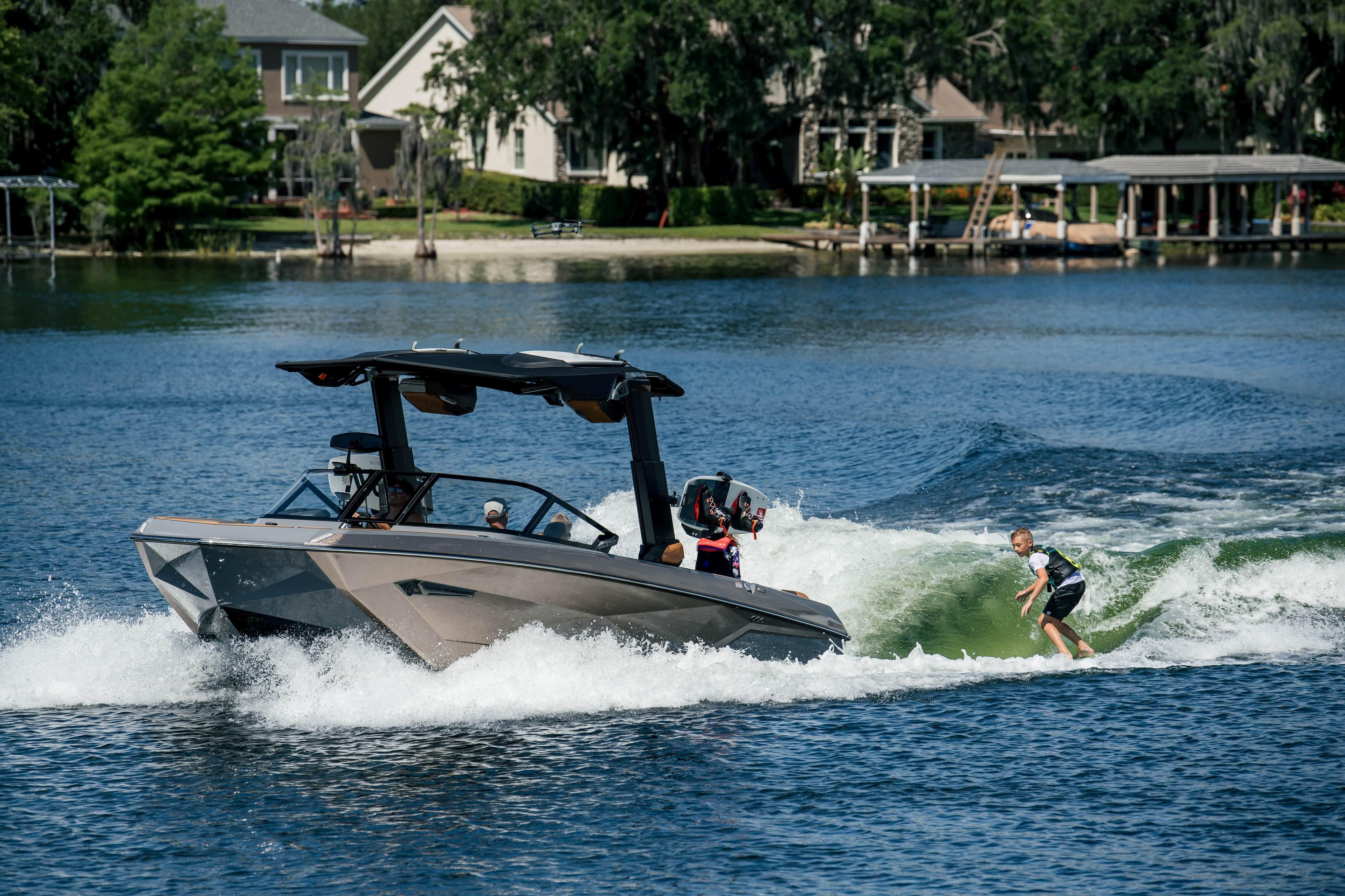 2026 Nautique G25 boat creating waves for a wakeboarder on a scenic lake.
