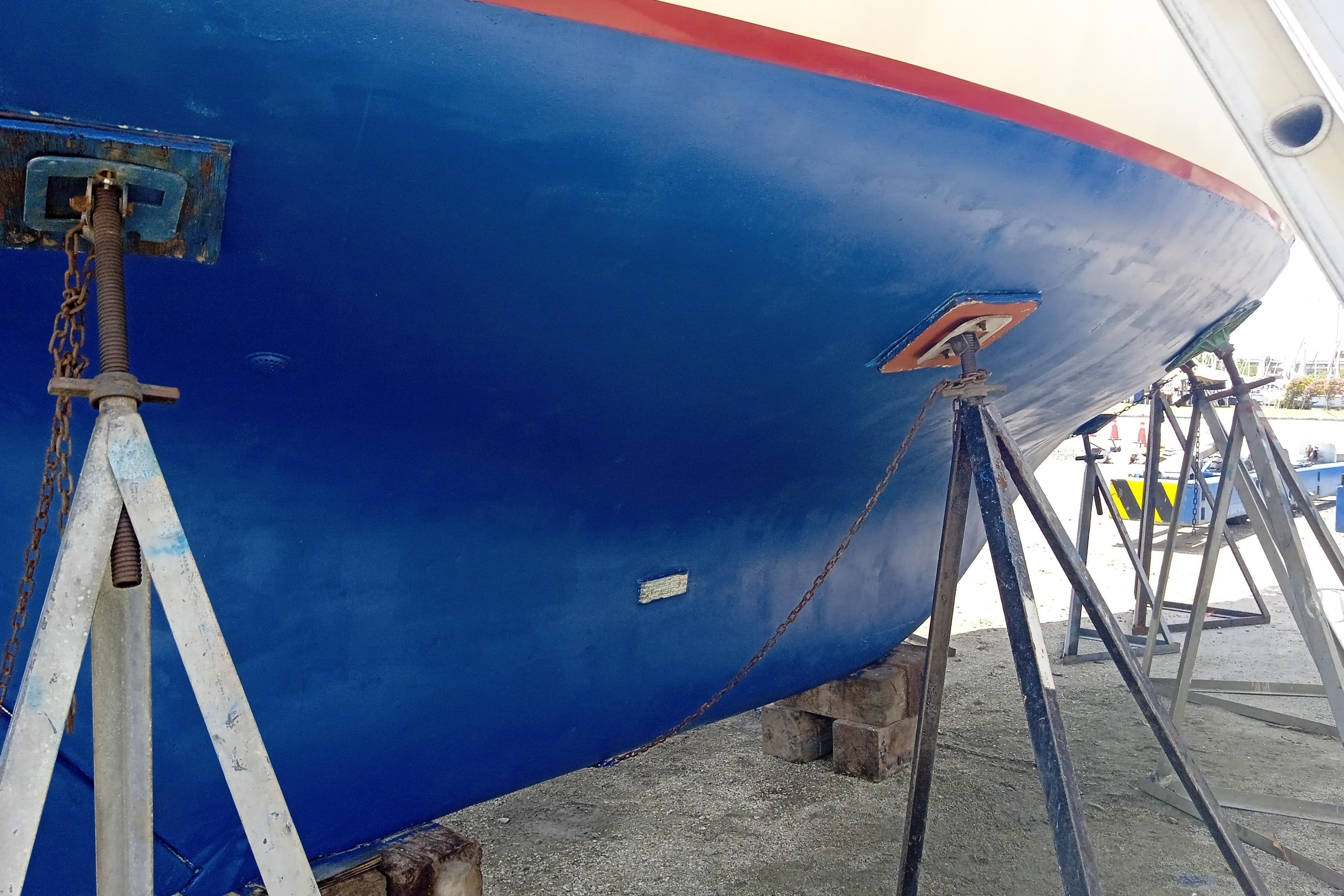 1983 Cape Dory 36 sailboat hull on stands, blue with red trim, in dry dock.
