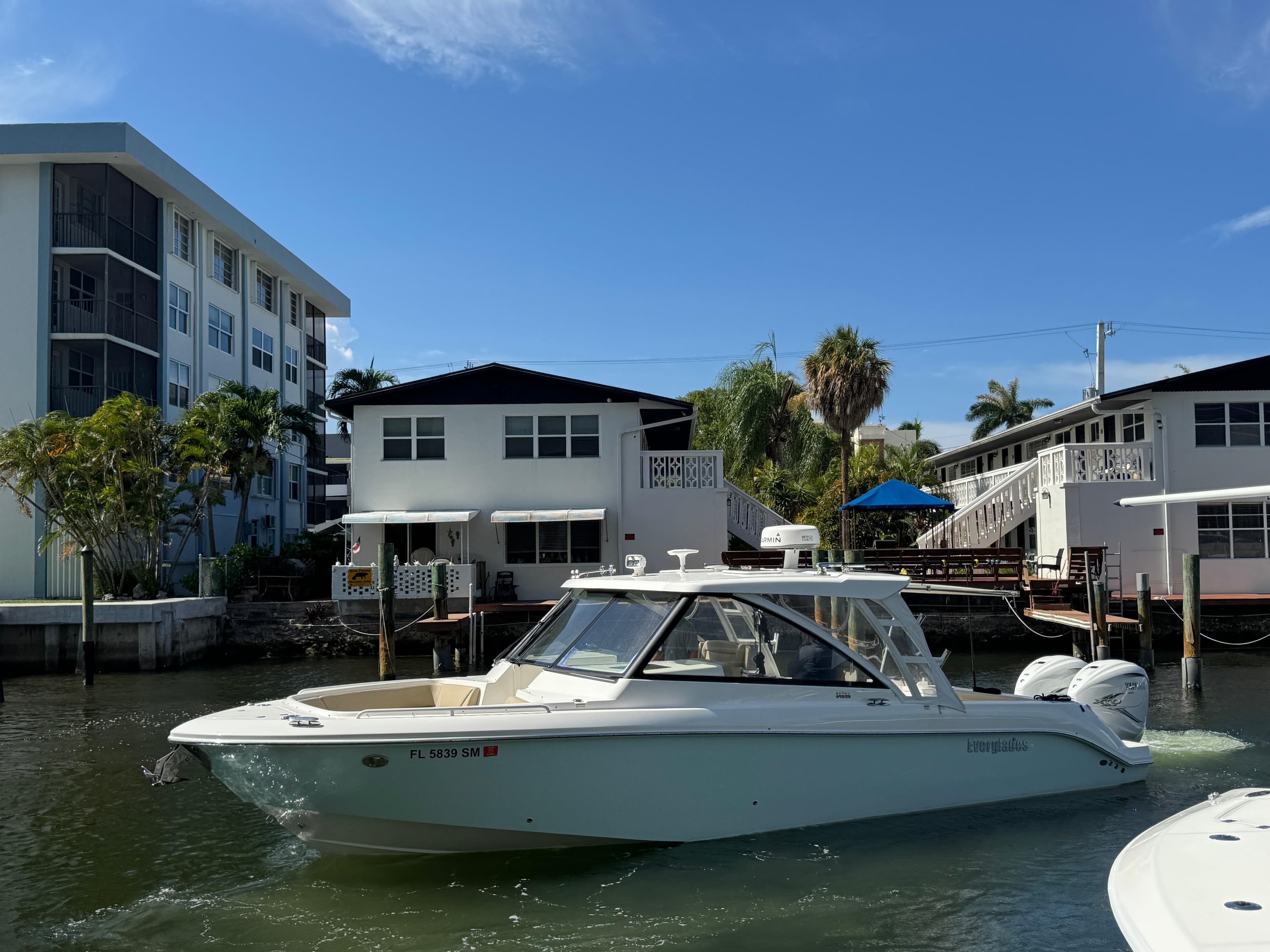 2019 Everglades 340 Dual Console boat cruising near waterfront homes under a clear blue sky.