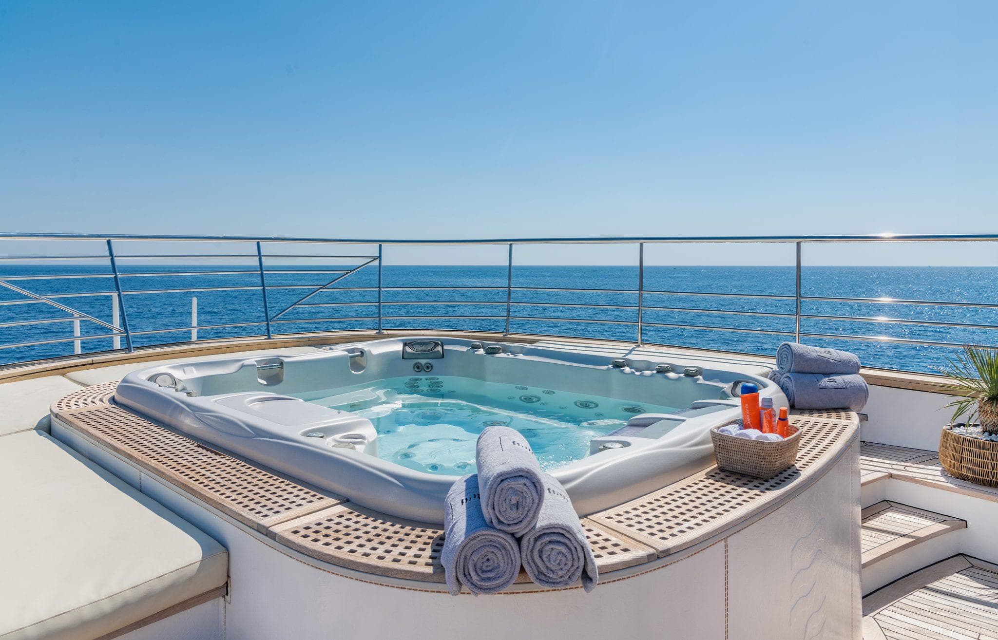 Luxurious yacht deck with jacuzzi, towels, and ocean view under clear blue sky.