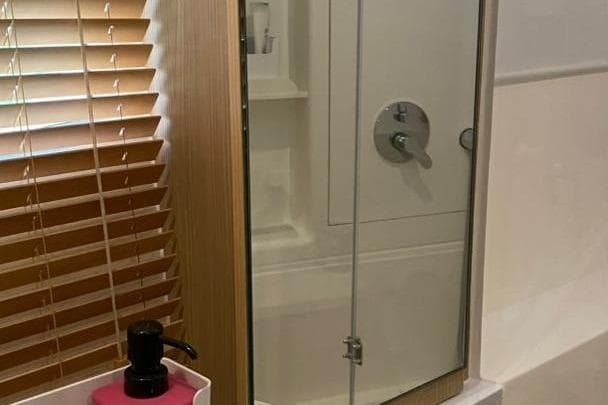 Modern bathroom with glass shower door, wooden blinds, and pink soap dispenser. Aquila 42, 2023 model.
