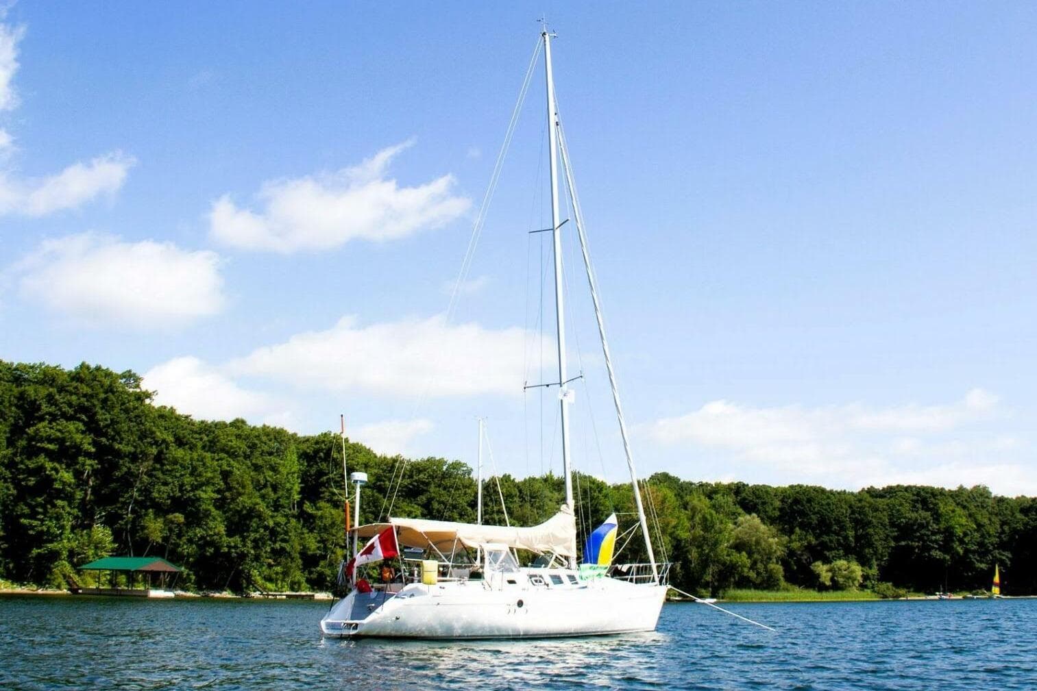 1989 Beneteau First 35s5 sailboat anchored on a serene lake with lush green trees.