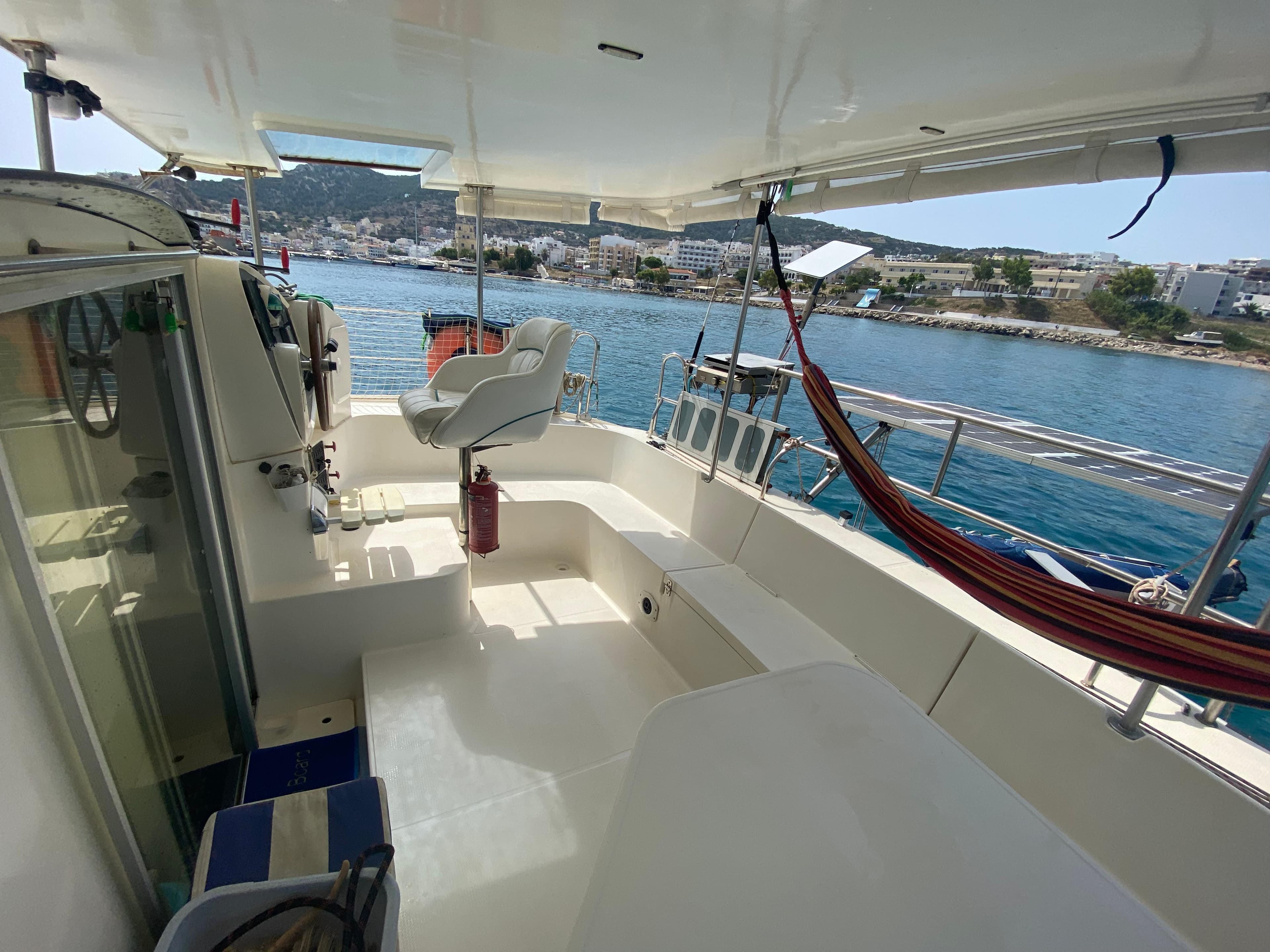 1999 Fountaine Pajot Athena 38 catamaran deck with seating, overlooking a scenic harbor.