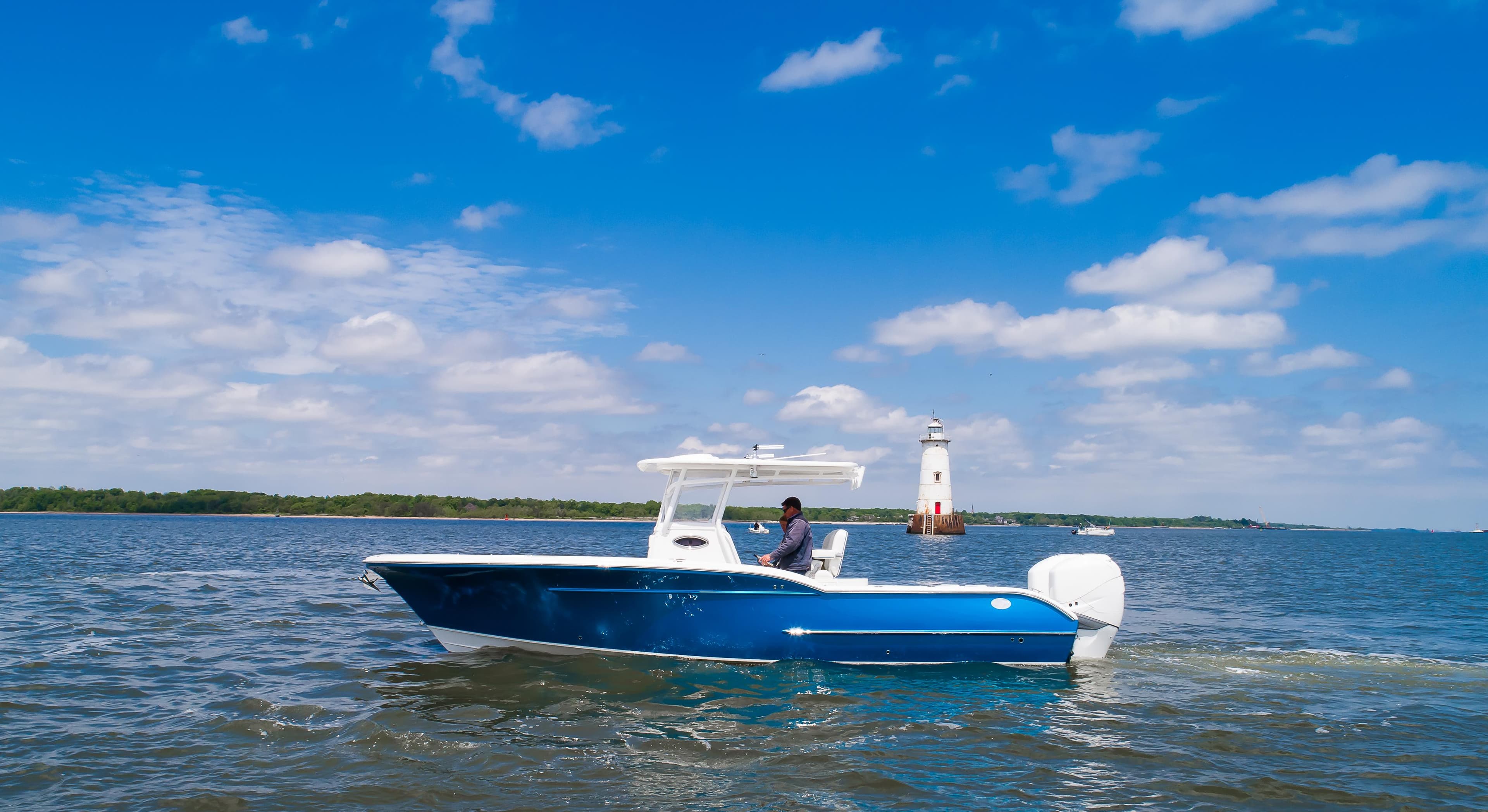 2025 Buddy Davis 28 Center Console boat cruising near a lighthouse on a sunny day.