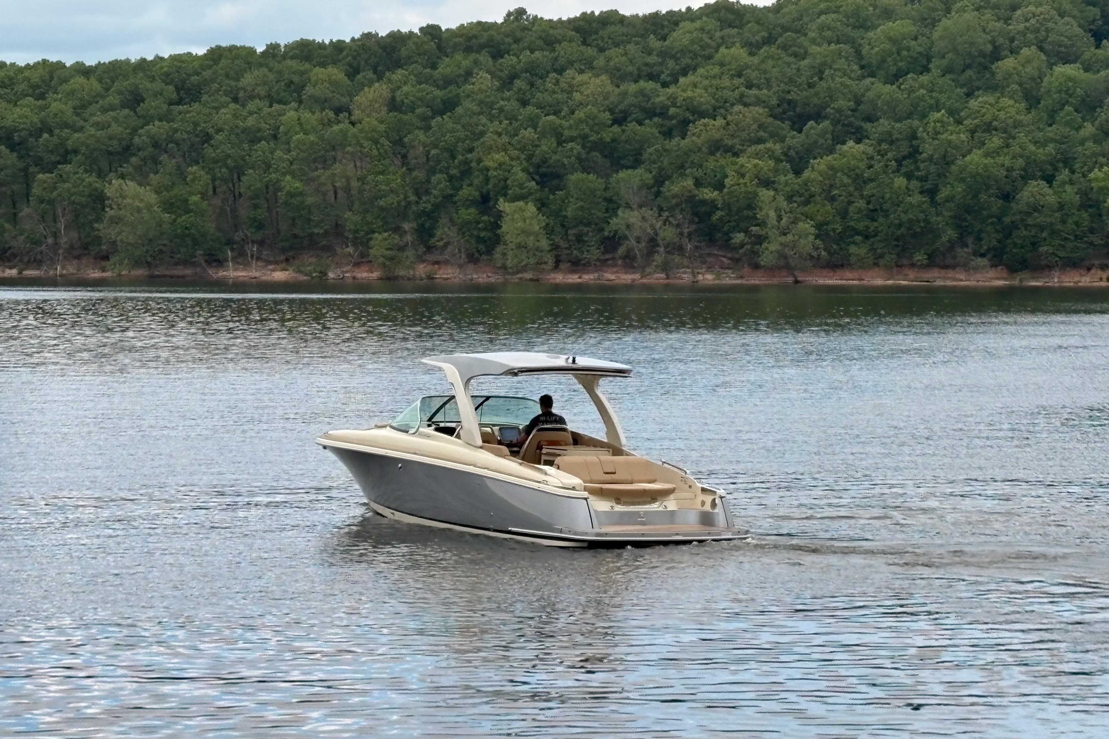 2026 Chris-Craft Launch 31 GT cruising on a serene lake with lush forest backdrop.
