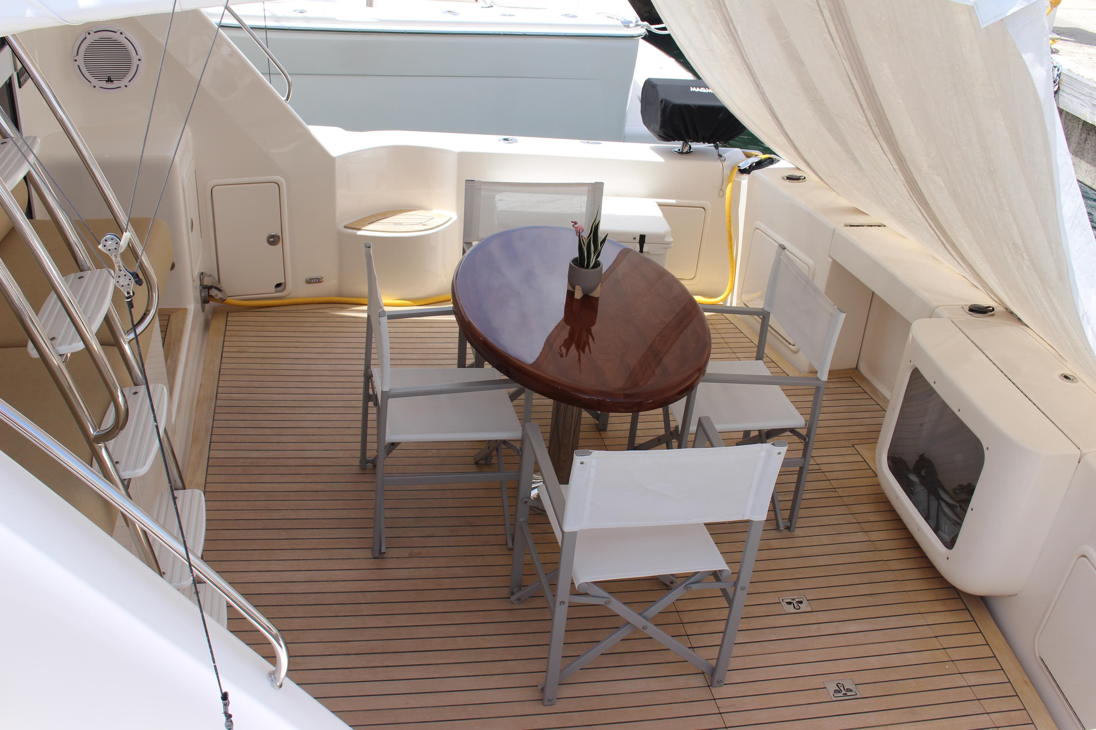 Outdoor seating area on a 2005 Riviera 51 Flybridge yacht with a wooden table and chairs.