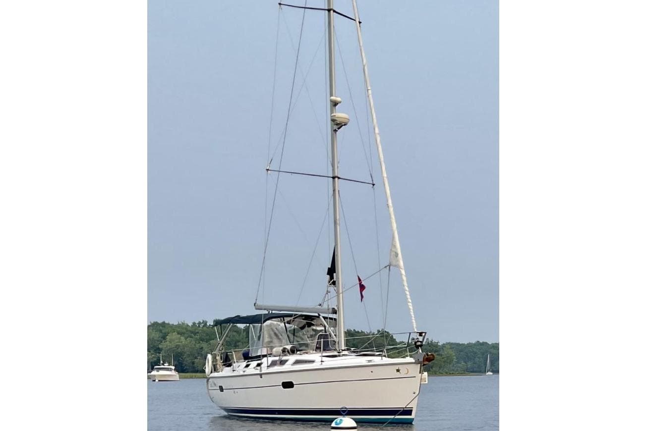 2004 Hunter 36 sailboat anchored on calm water with forested background.