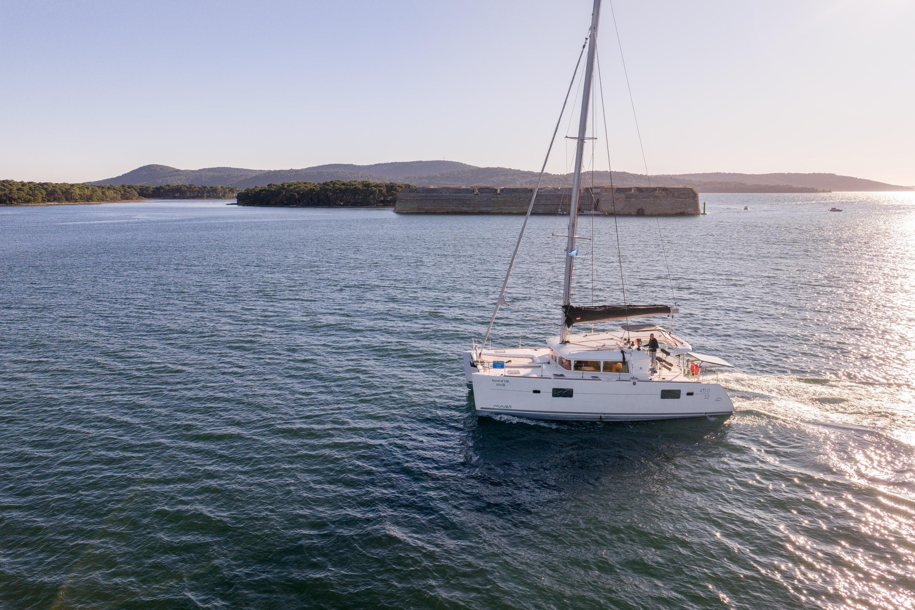 Sailing Lagoon 400 S2 catamaran, 2015 model, on serene waters with distant hills.